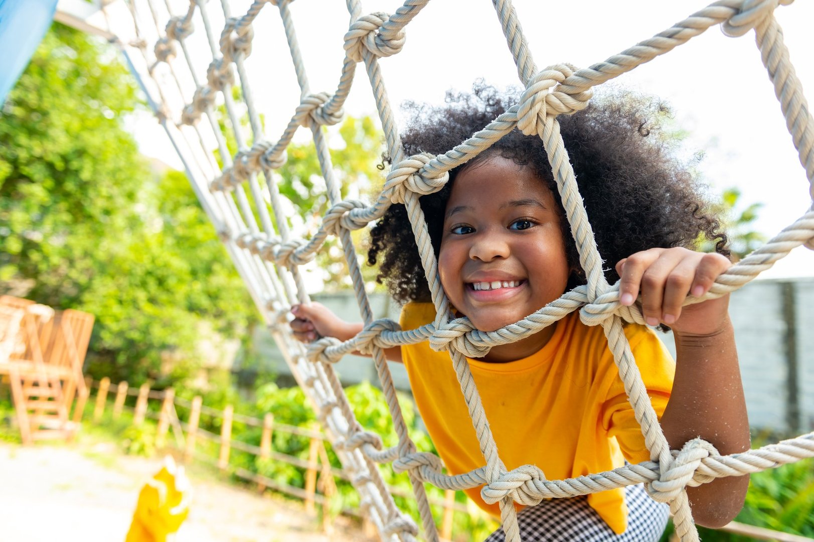 Happy Little African child girl playing and climbing rope net at outdoor playground in the park on summer vacation. Kindergarten children kid enjoy and fun outdoor activity and exercising at park.