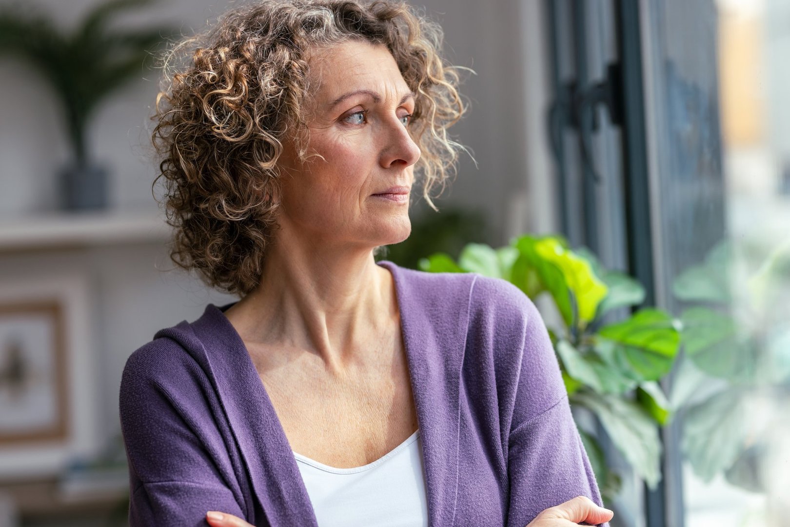 Portrait of serious mature woman looking forwards near the window in the living room at home
