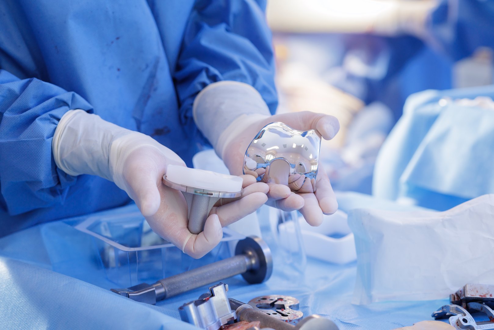 Orthopedic surgeon shows knee replacement implant parts on a sterile drape during arthroplasty preparation, ideal for medical education and marketing