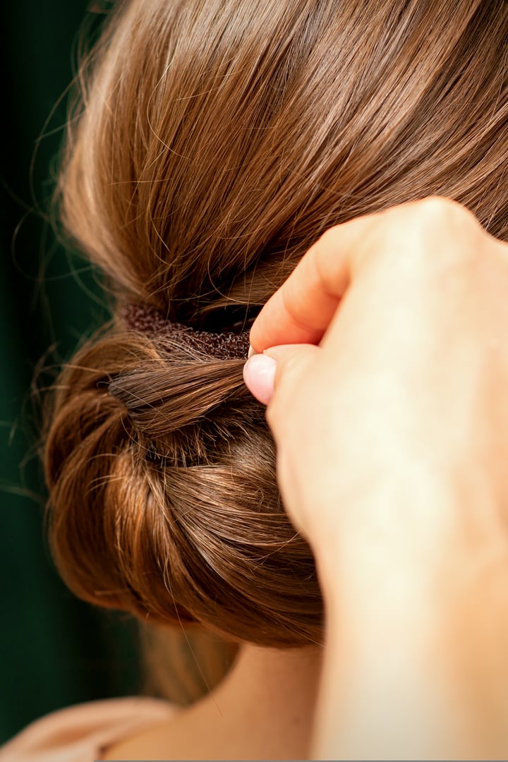 Hands of hairdresser making french twist hairstyle of an unrecognizable young brunette woman in a beauty salon, back view, close up