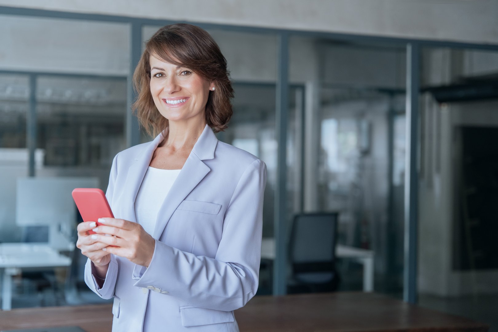 Portrait of mature businesswoman CEO holding smartphone using fintech app looking at camera in office. Smiling Latin Hispanic adult professional business woman using mobile phone cellphone. Copy space