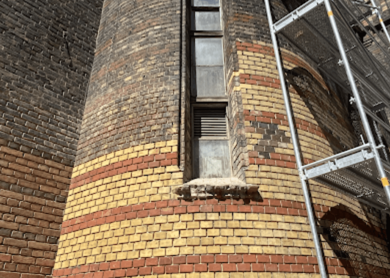 A worker removes rust and corrosion from a metal surface using a wire brush attachment on an electric drill.