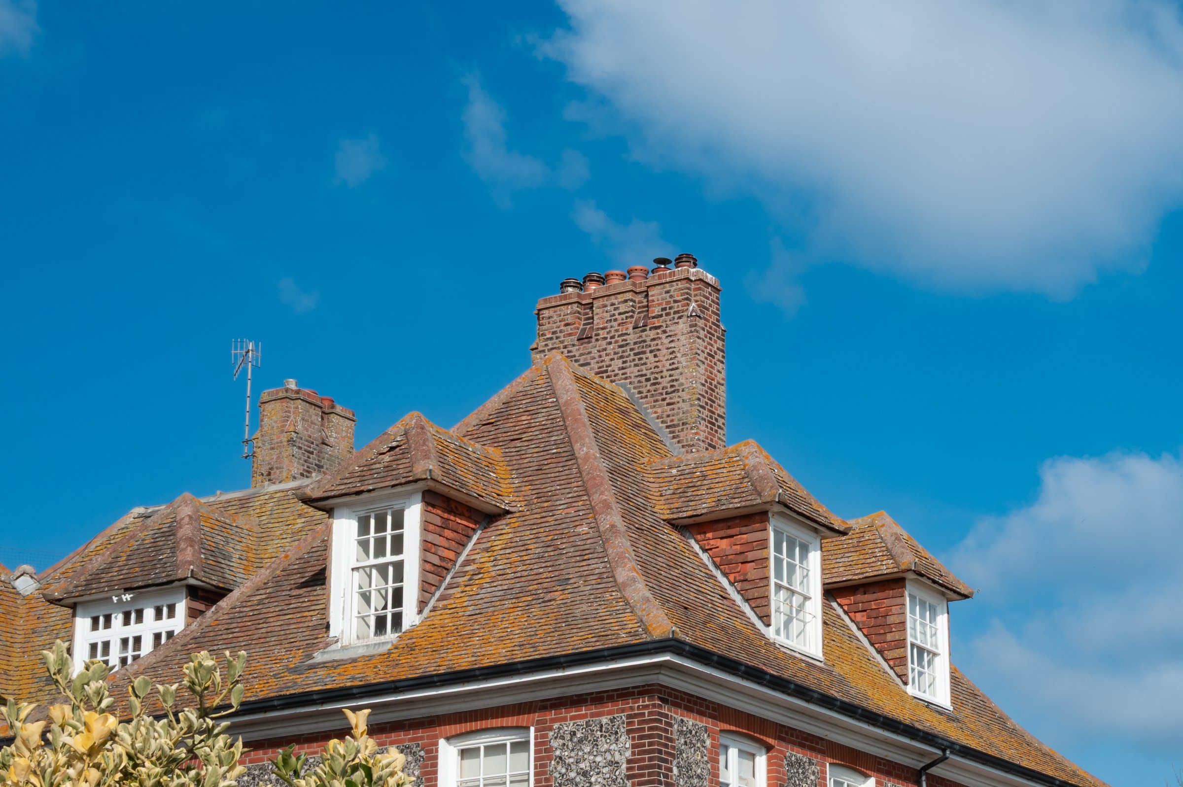Roof top view of a large, turn of the century English house showing its dorms windows, large chimney and various sash windows. Overlooking the sea in the east of the country.