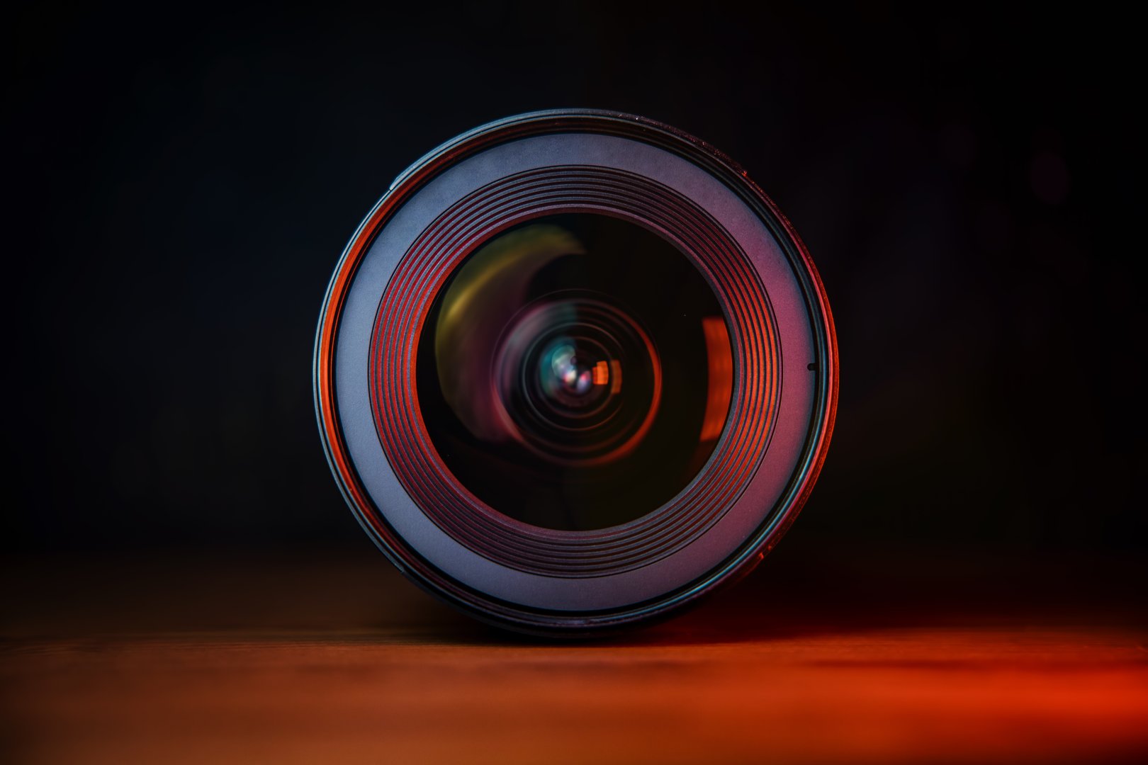 Photograph of a camera lens with concentric details, filmed against a moody black and orange background, creating a dramatic and professional visual aesthetic.