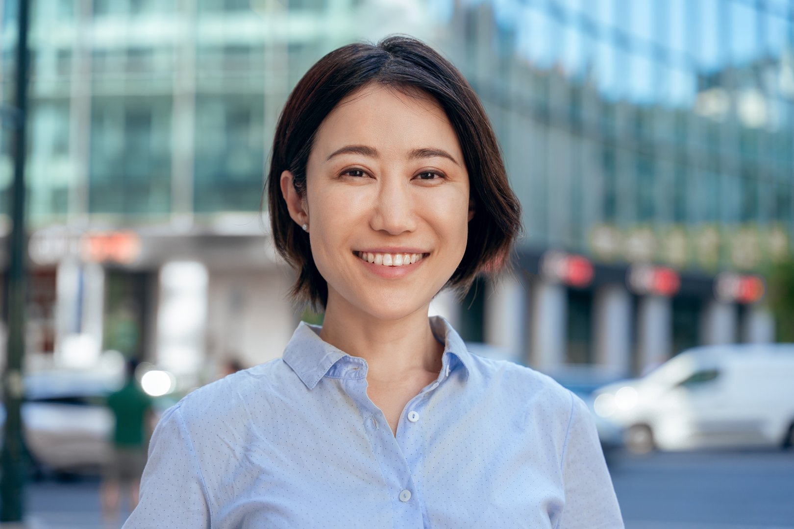 Closeup headshot face portrait of mature Asian executive sale manager business woman looking at camera outdoors. Smiling female entrepreneur ceo leader businesswoman on busy city street background