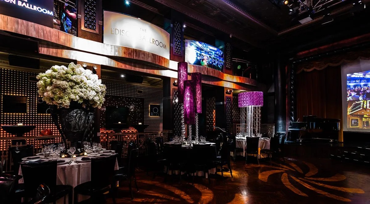 Elegant ballroom with ornate decorations, tables set with floral centerpieces, and vibrant lighting in a luxurious setting.