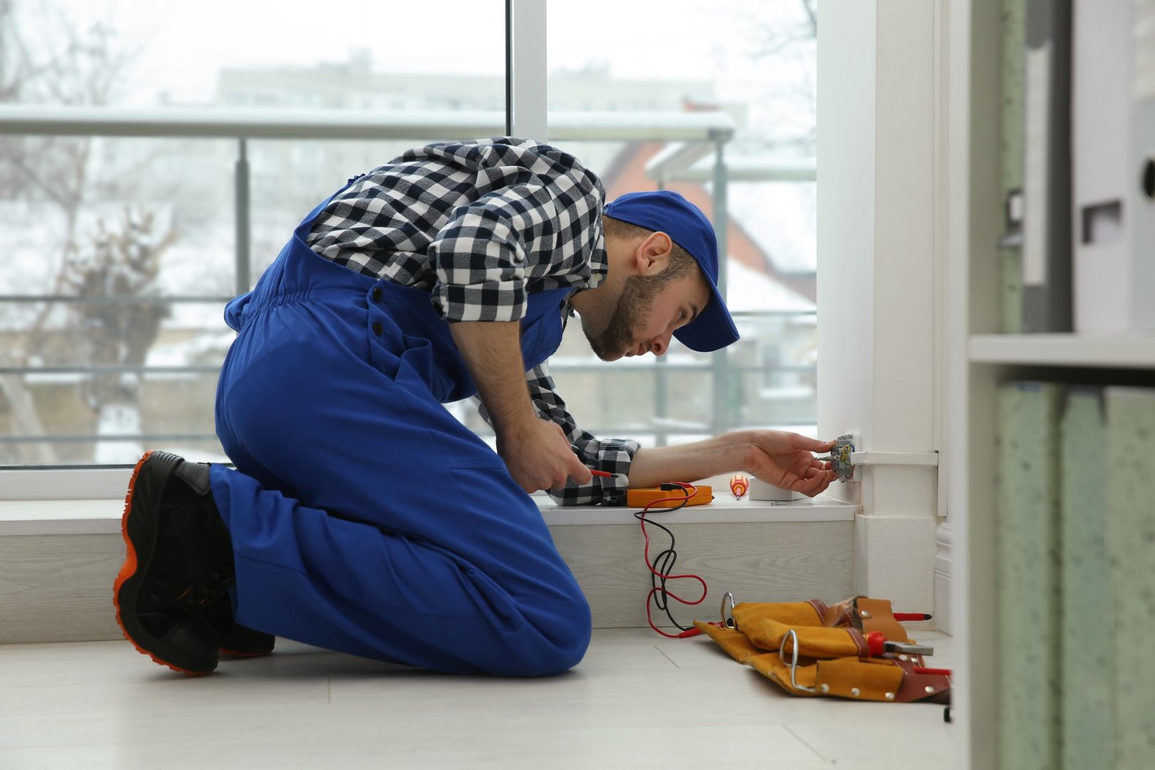 Electrician with screwdriver repairing power socket indoors