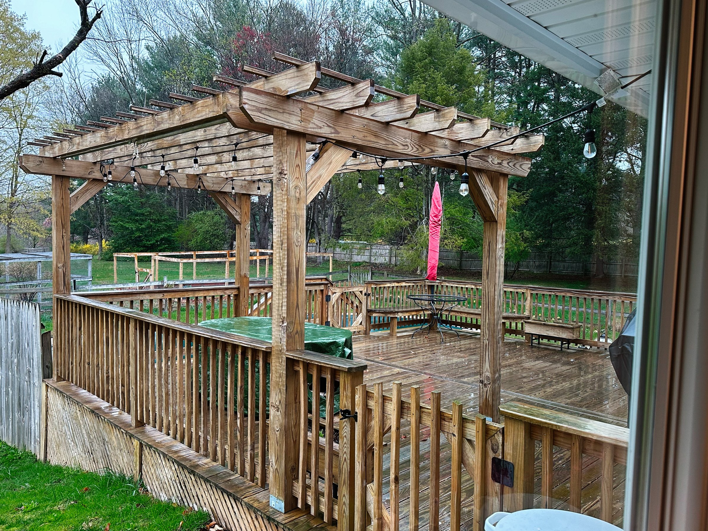 Jenkintown, Pennsylvania, USA - April 25, 2025: Rainy backyard deck under a wooden pergola with string lights and outdoor furniture in the USA.