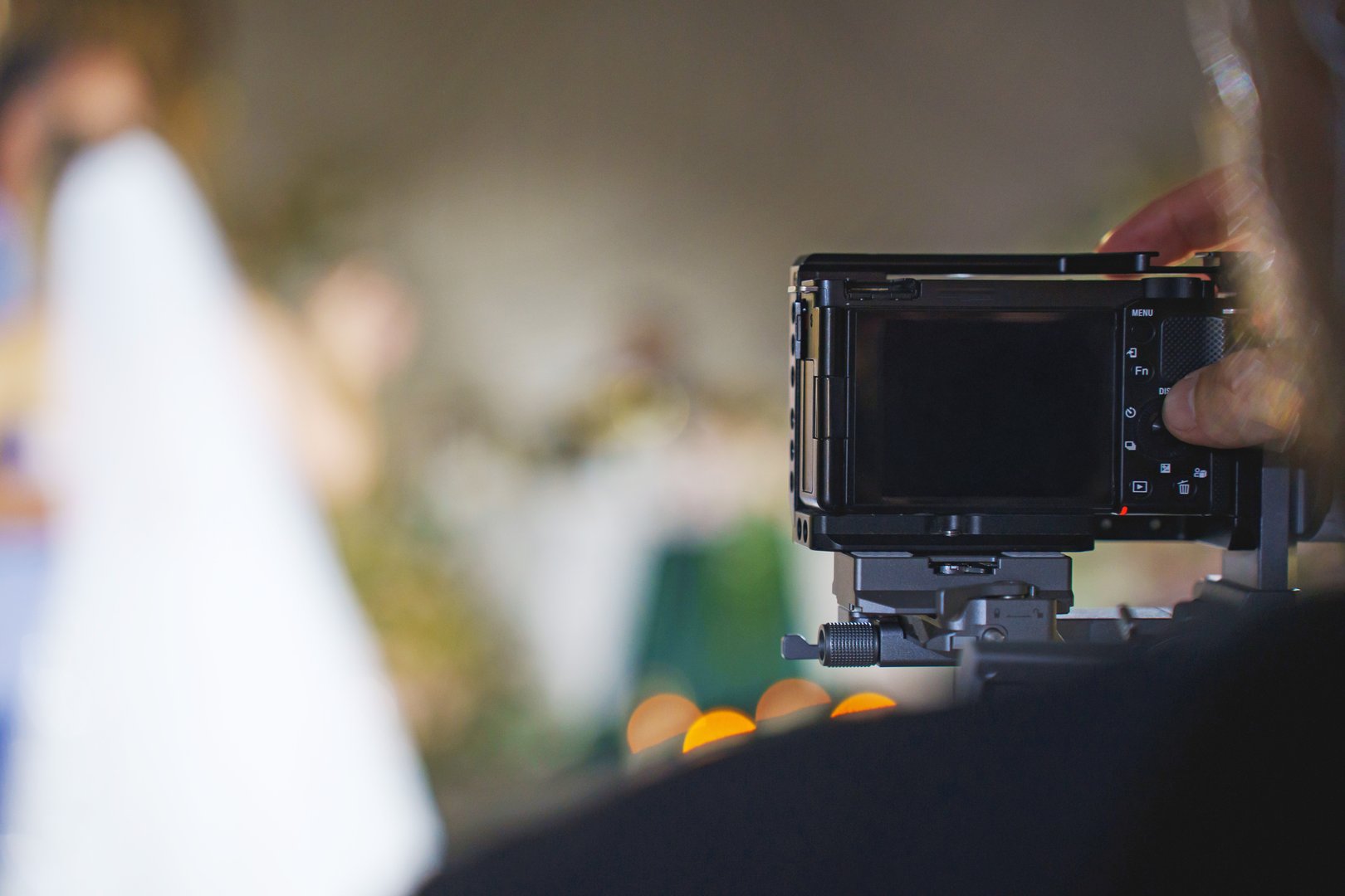 A photographer focuses on a couple during their wedding ceremony. The scene is warm with beautiful decor and guests in the background celebrating love.
