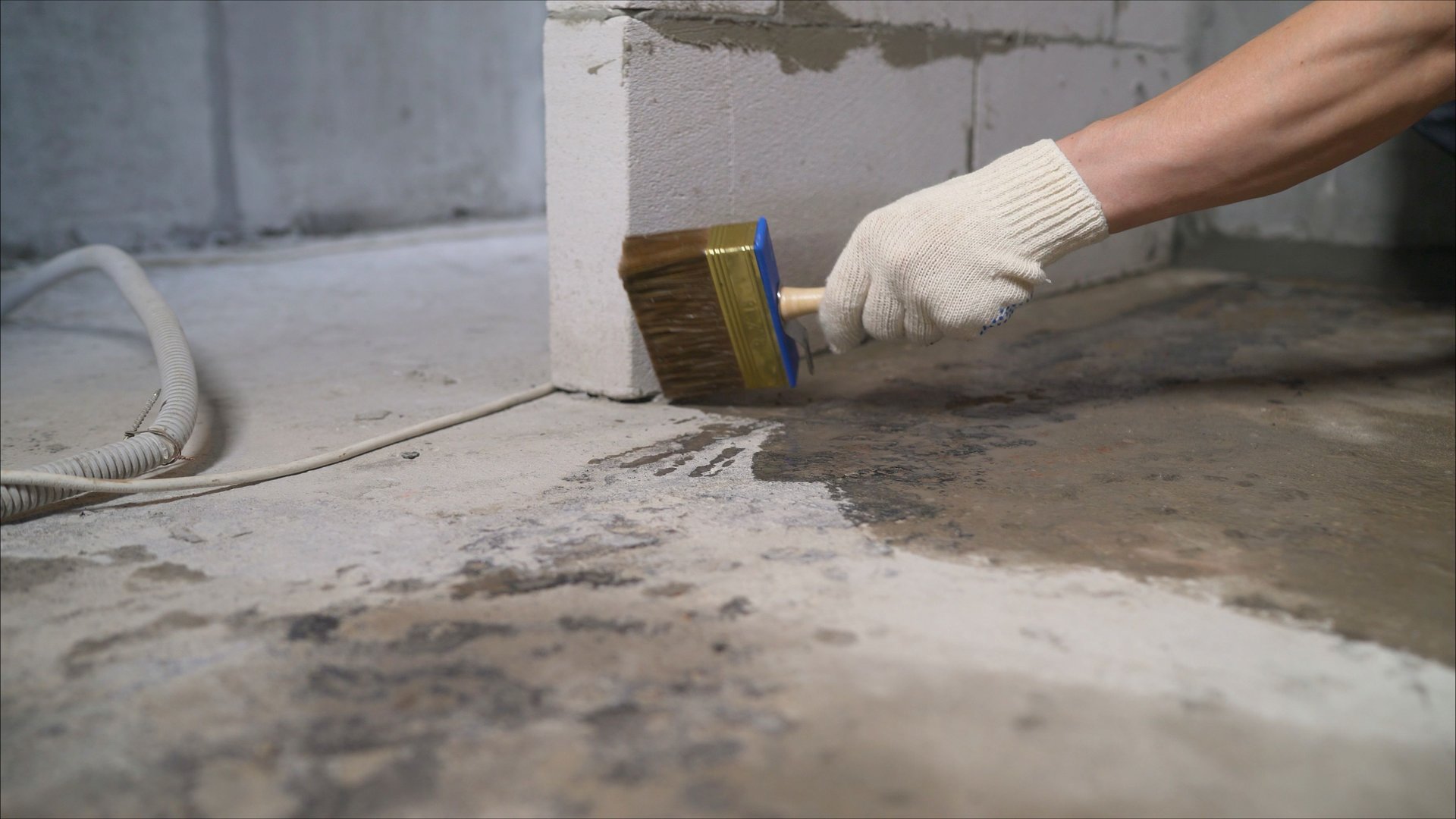 Construction worker waterproofing concrete floor using a brush