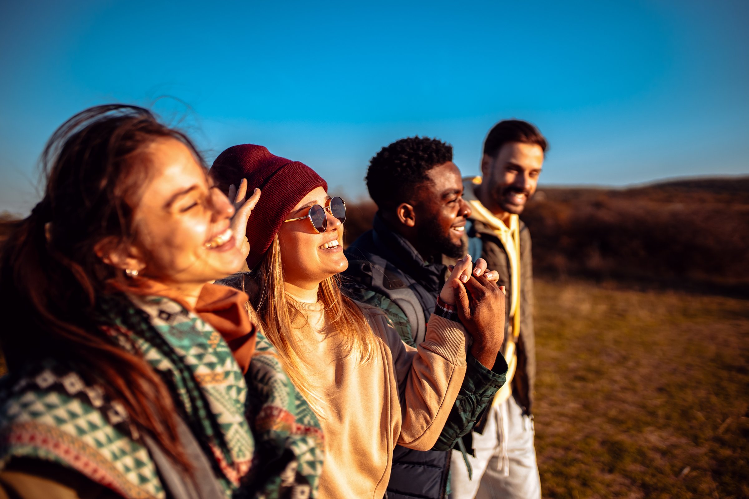Smiling group of friends having fun while hiking together on hill at sunset.