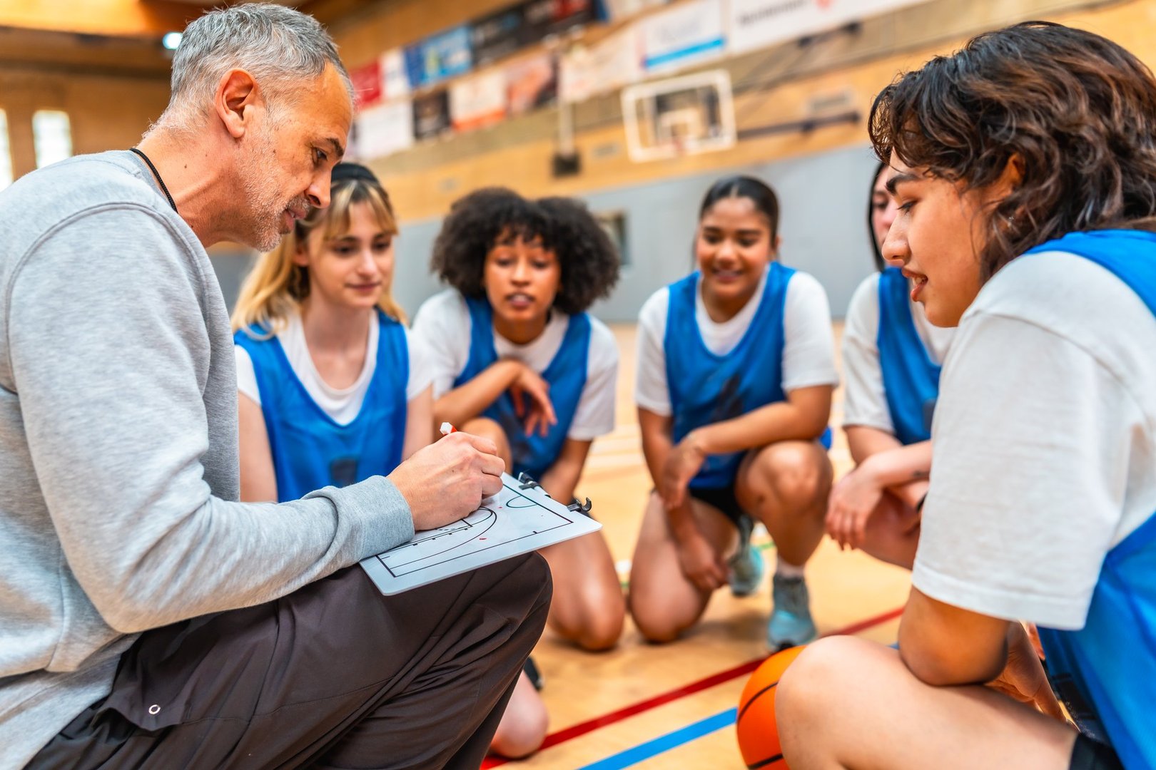 Basketball coach drawing a play on a clipboard and explaining game strategy to a group of young female athletes