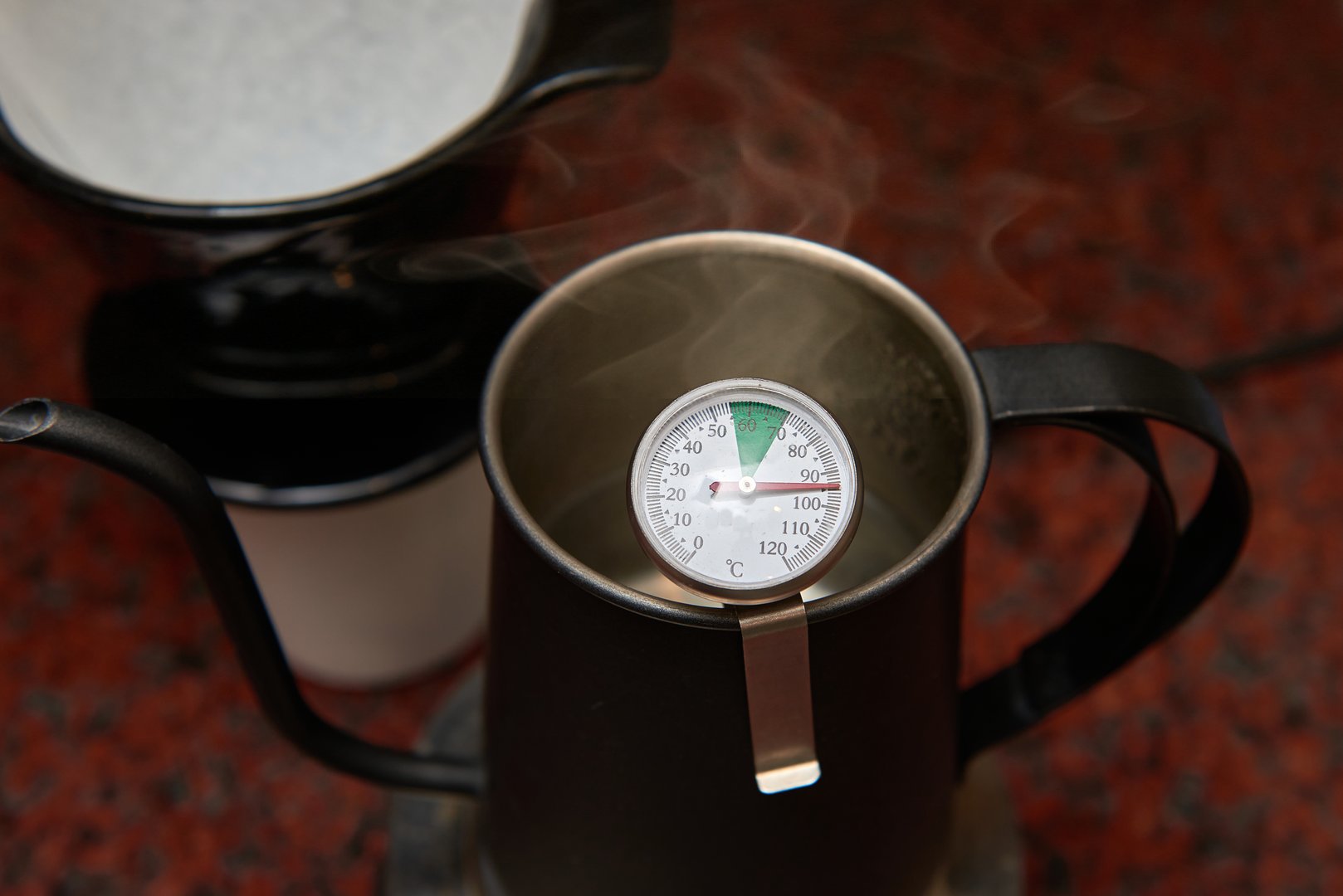 A detailed macro of a thermometer in a steaming kettle, indicating the ideal water temperature for specialty coffee. A concept for the science, precision, and craft of a professional barista.