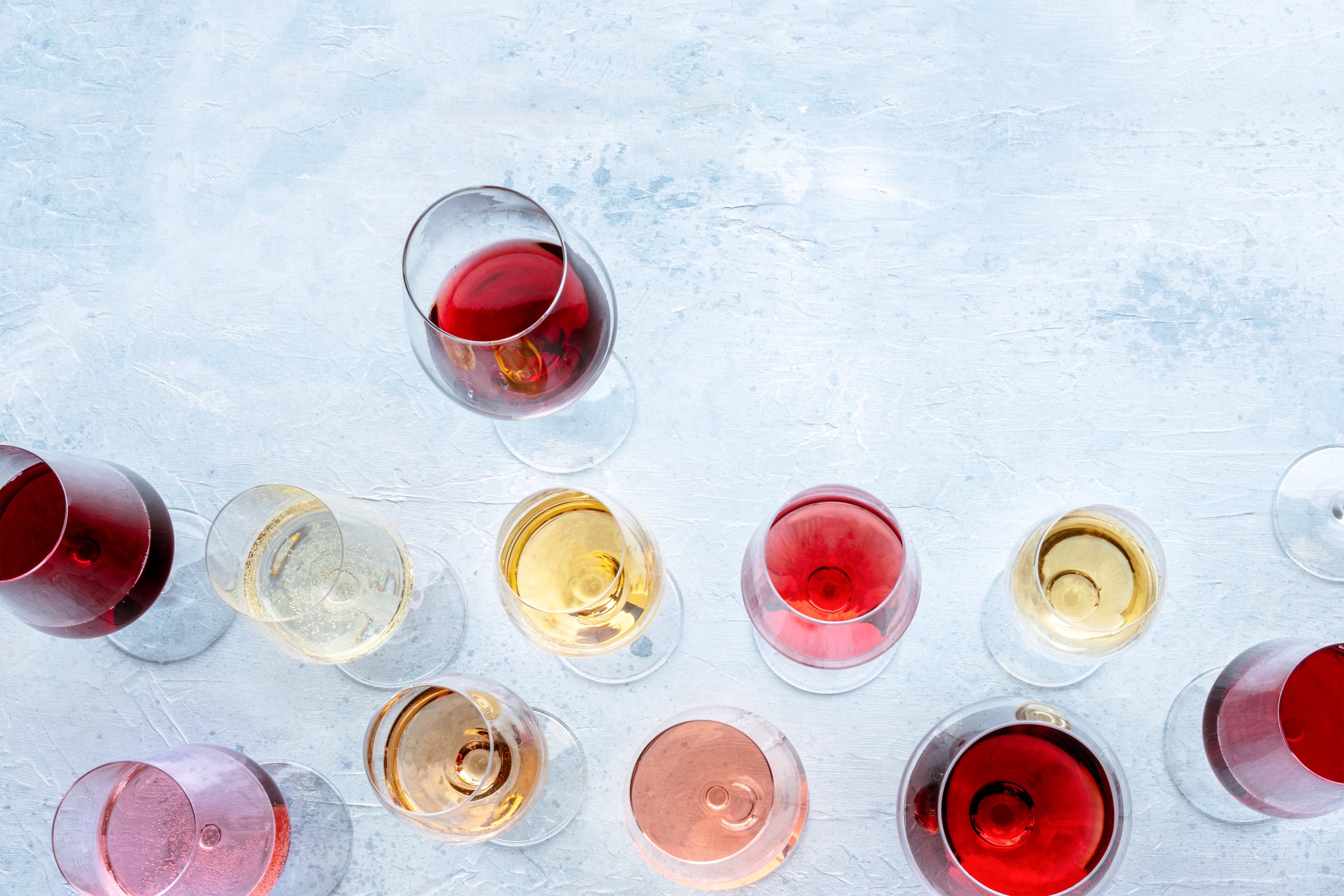 Wine glasses at a tasting. Rose, red, and white wine, drinks on a table at a winery, shot from the top. An assortment of wines of many different colors