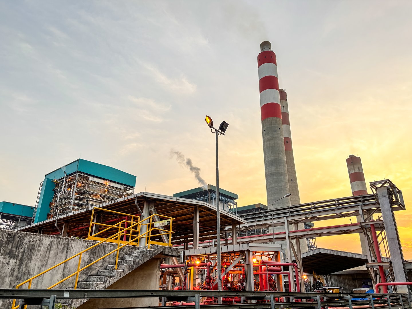 Industrial power plant landscape with chimneys, infrastructure, and yellow sunset sky at dusk