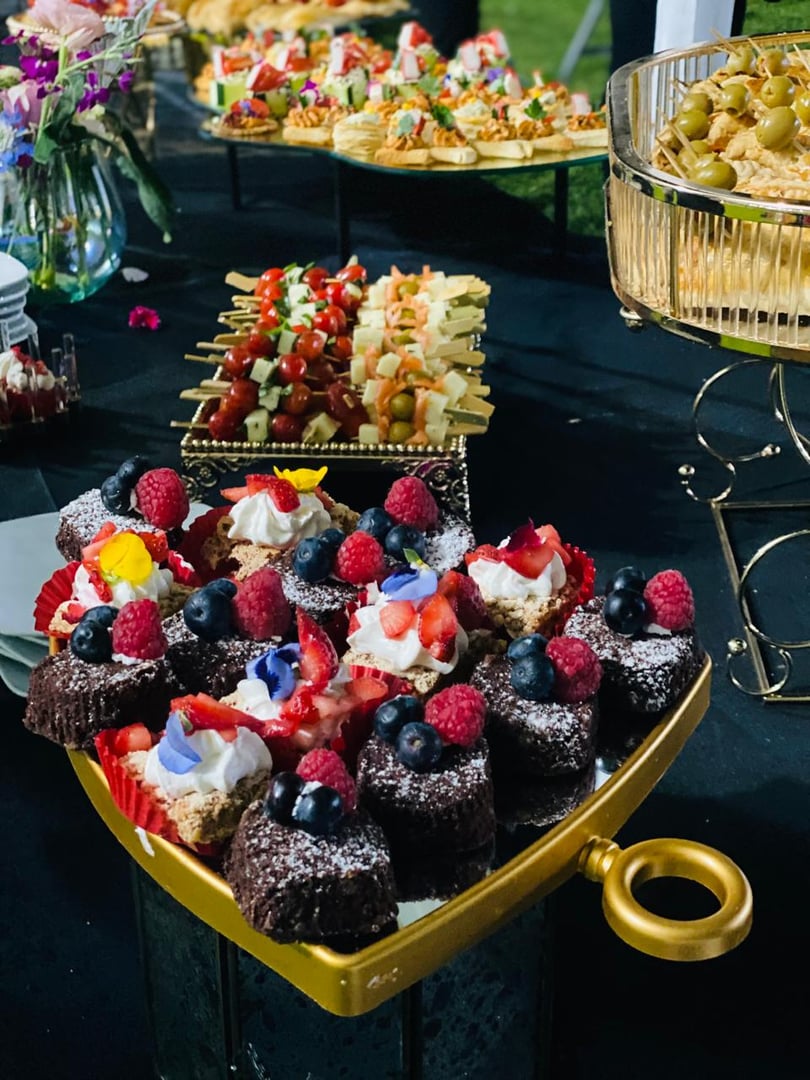A variety of elegant desserts and appetizers displayed on a black table, featuring fruit-topped pastries and skewered snacks.