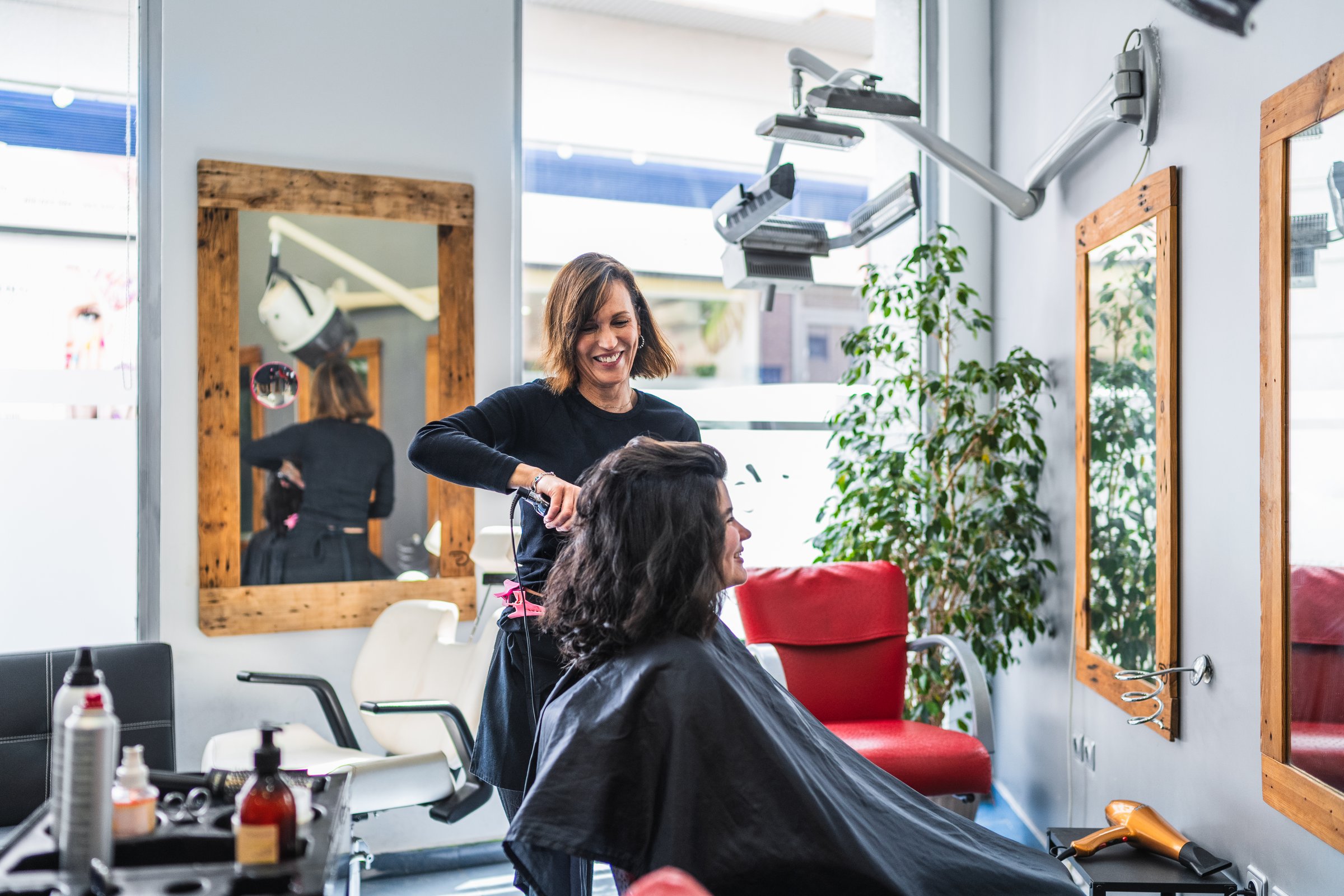 A hairdresser styles a client's hair in a modern salon featuring large mirrors. The setting is stylish and professional. Concept of stylish hair salon.