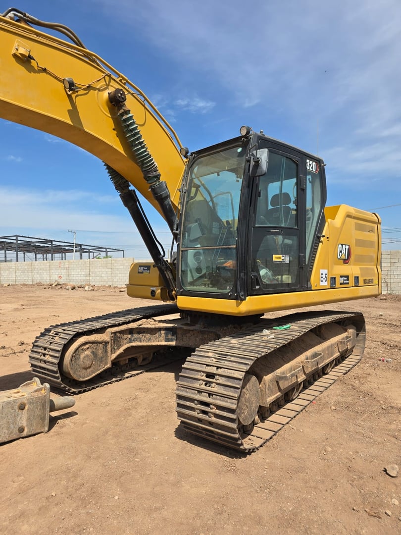 Yellow excavator with caterpillar tracks on a construction site, featuring a clear sky and industrial background.