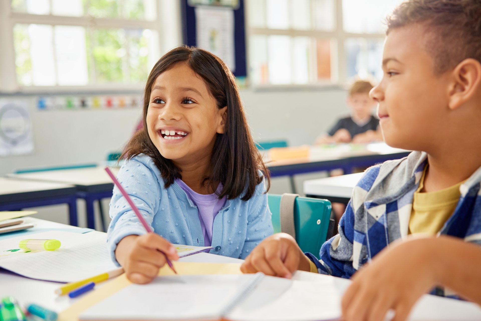 Cheerful and helpful middle eastern schoolgirl assisting classmate in studies during lesson. Cute girl and school boy studying together in classroom in school. Indian child working together with friend for a group task.