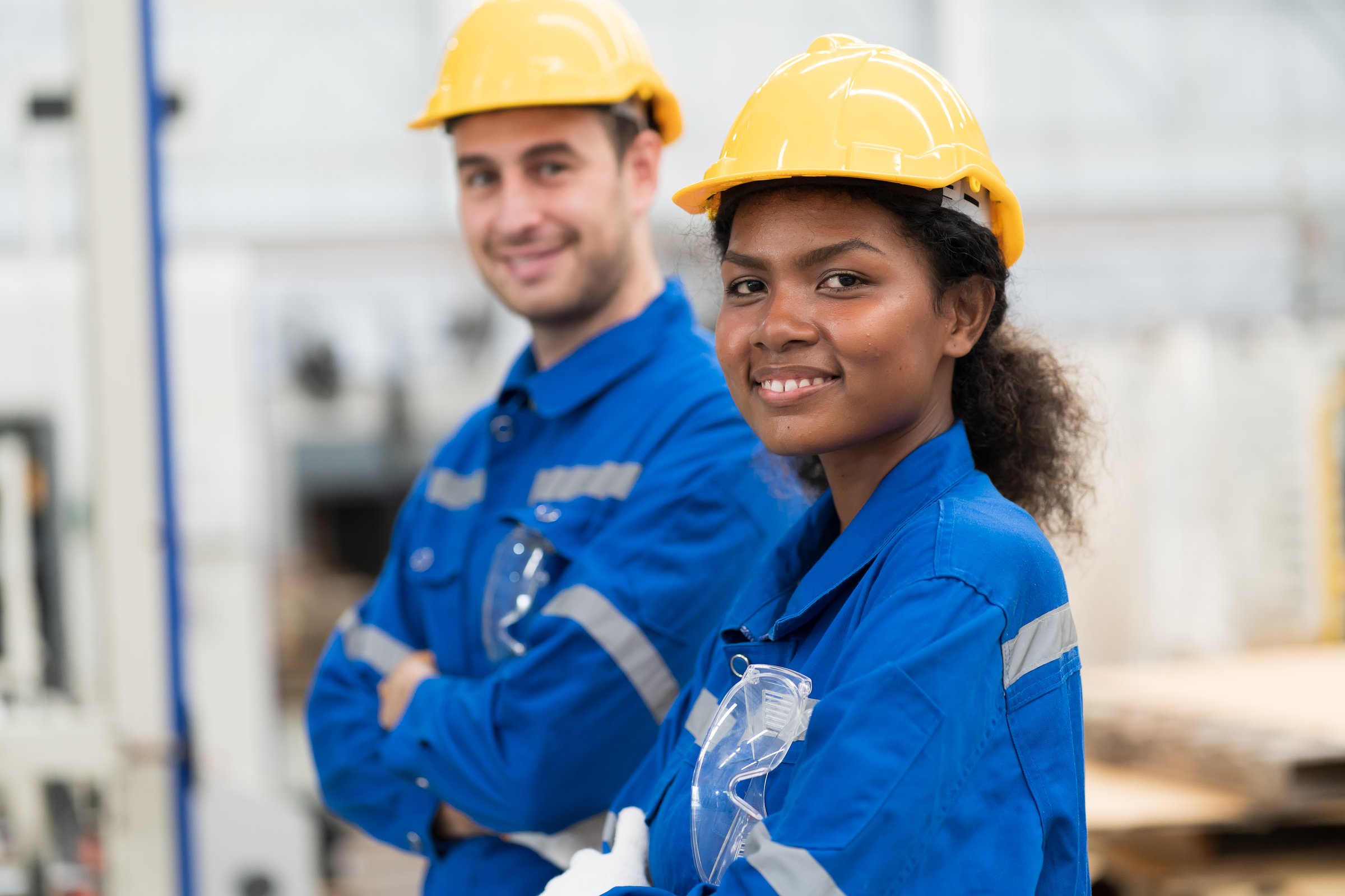 Male and female engineer worker wearing safety uniform and helmet standing with crossed arms in industry factory. Group of engineer at workplace. Team of engineer in line production
