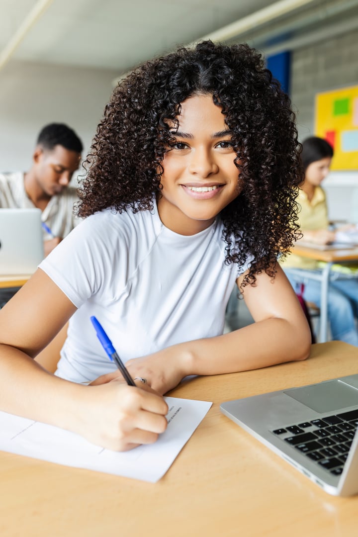 Portrait of young african american high school student smiling at camera while doing an exam at classroom. Education concept