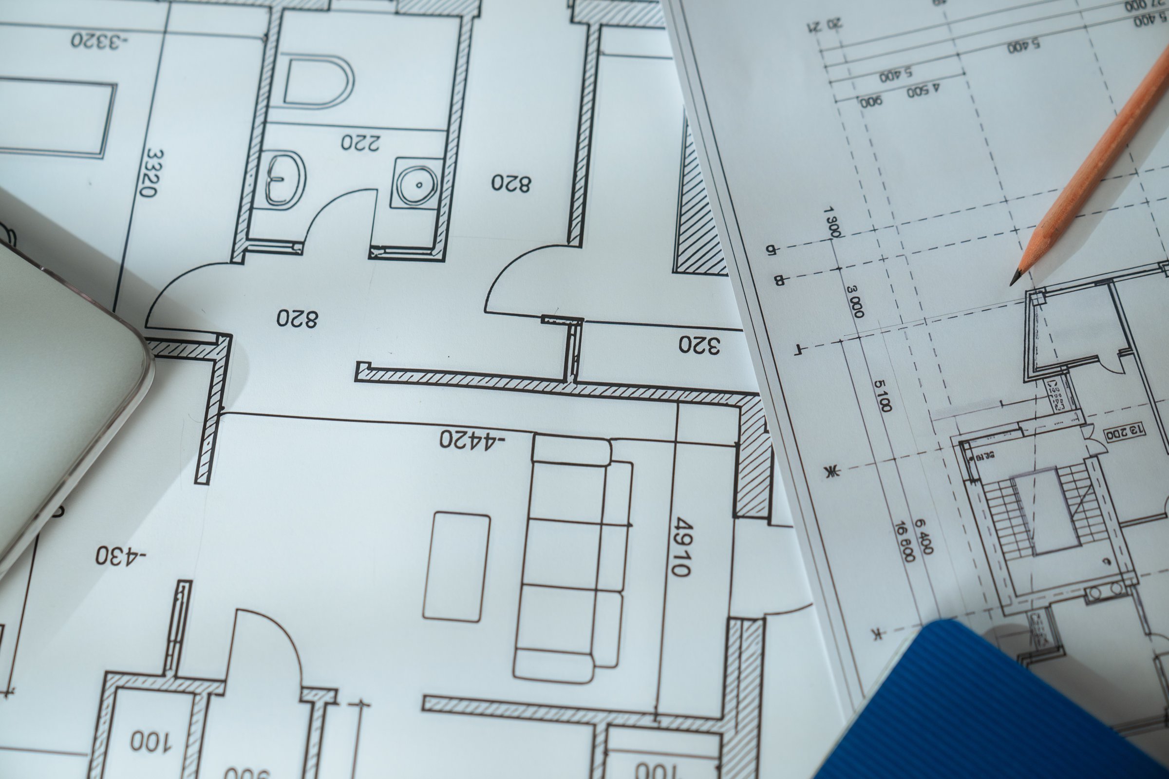 An architectural blueprint featuring detailed technical drawings, placed beneath a wooden ruler on a workspace.