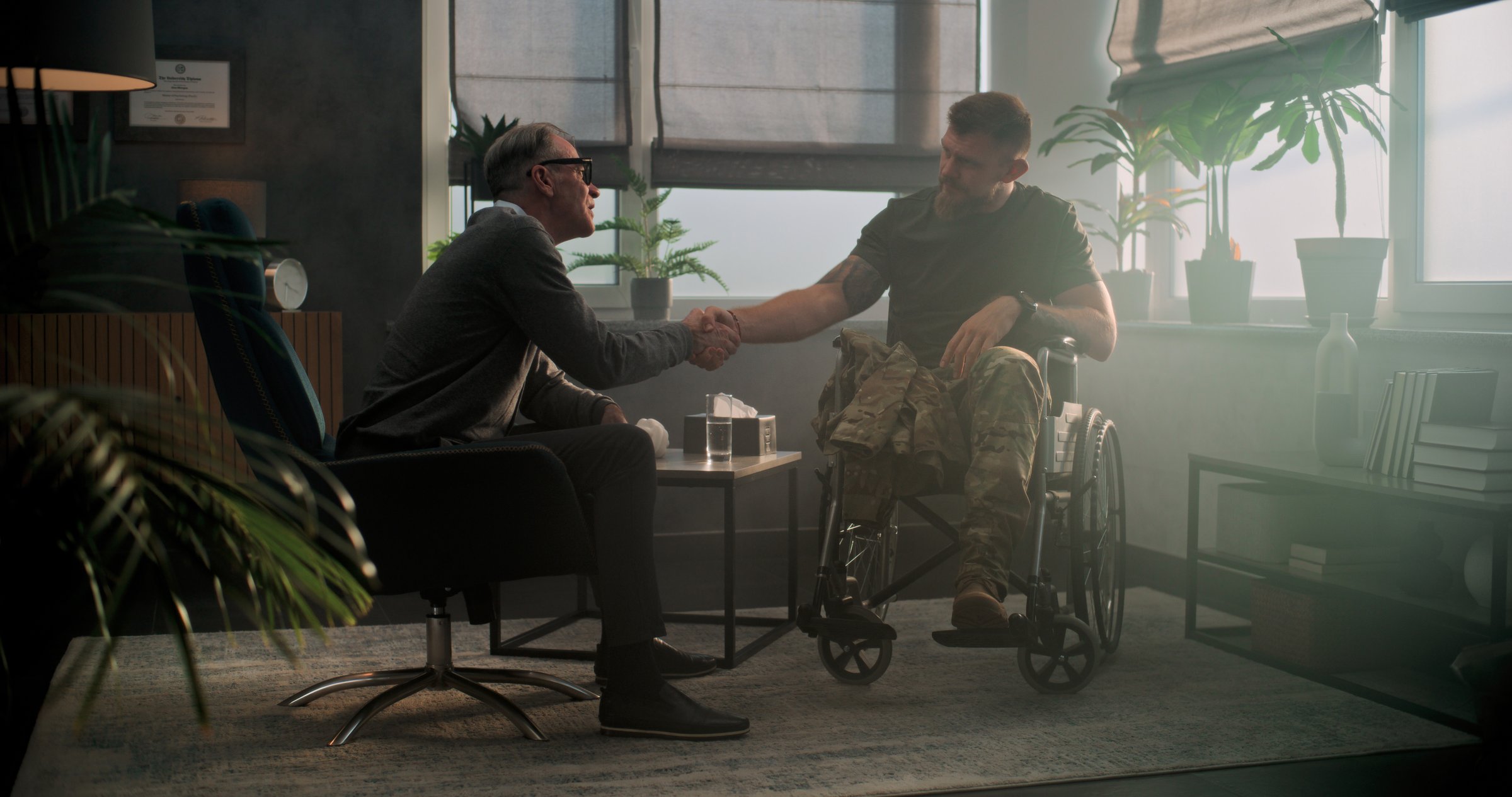 Senior psychologist supports military man with disability. Male soldier in wheelchair shakes hands with psychotherapist after therapy session or rehabilitation. Psychological help and mental health.