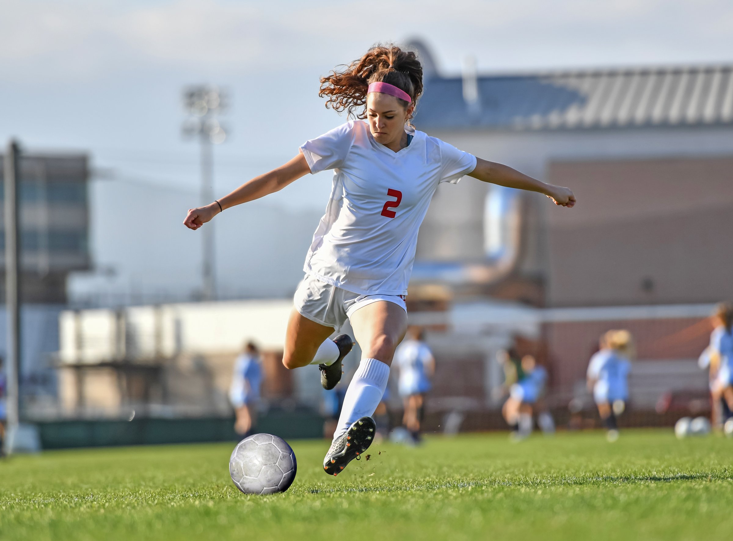 Very athletic young girl kicking and dribbling the soccer ball on a grassy green field.