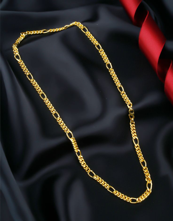 A gold chain necklace elegantly displayed on black satin fabric with a red ribbon accent.