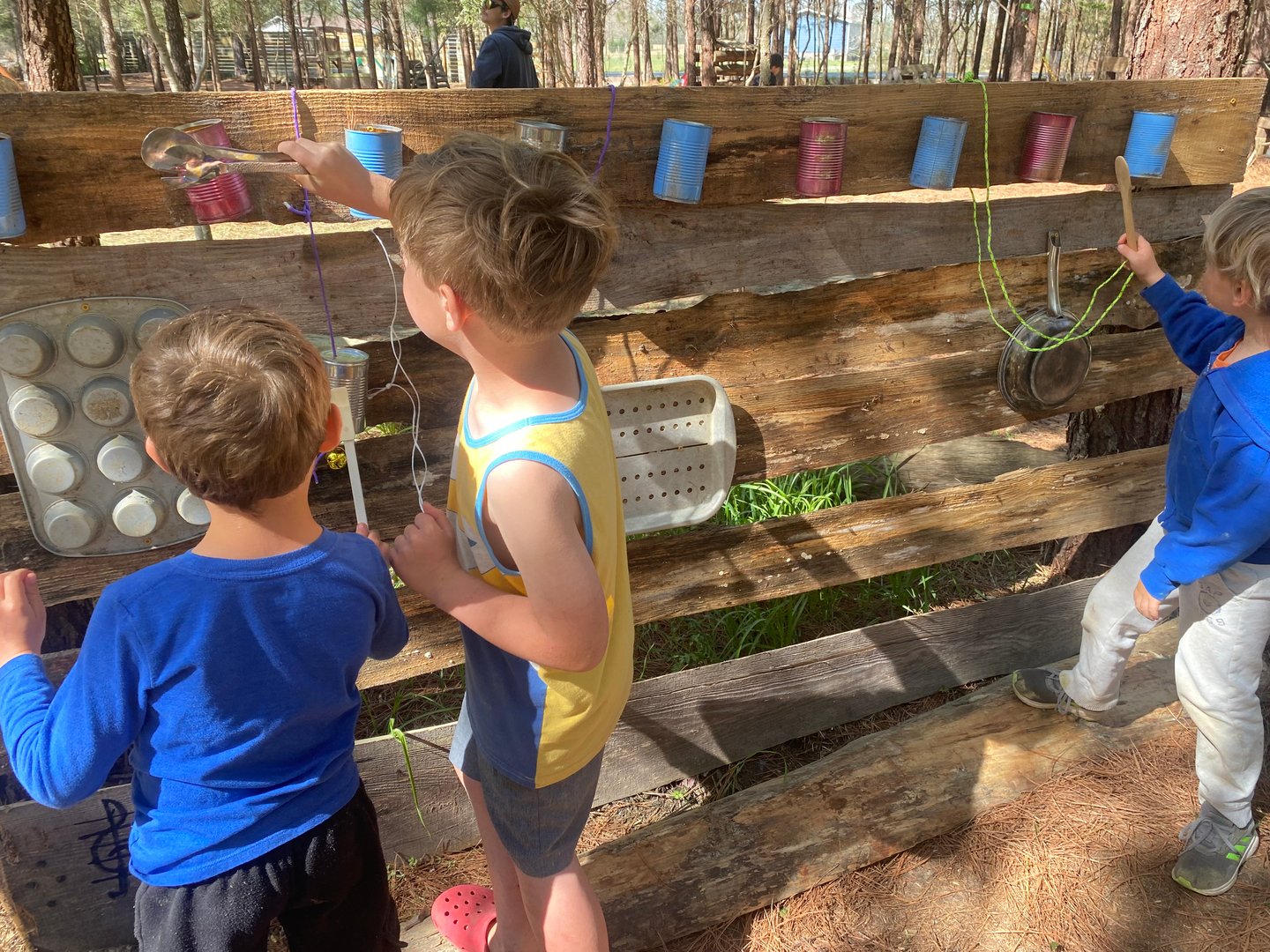 Children exploring a handmade outdoor music wall made from recycled materials at a nature-based Waldorf-inspired program