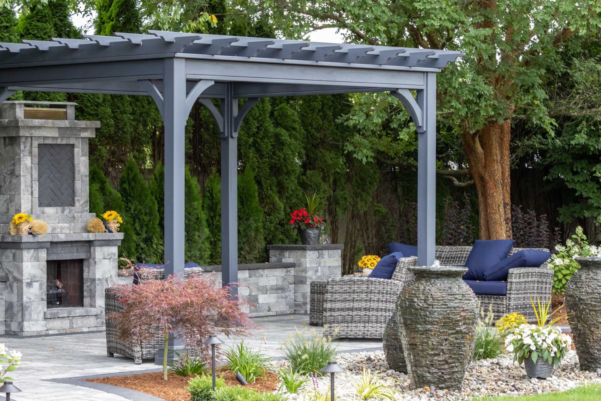 Landscape architecture featuring pergola and stone fireplace with stone urn water fountains for backyard patio oasis
