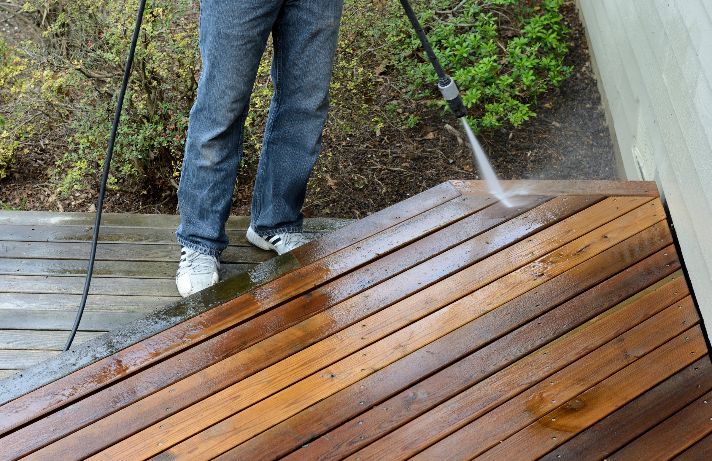 Man using pressure washer to clean cedar deck.