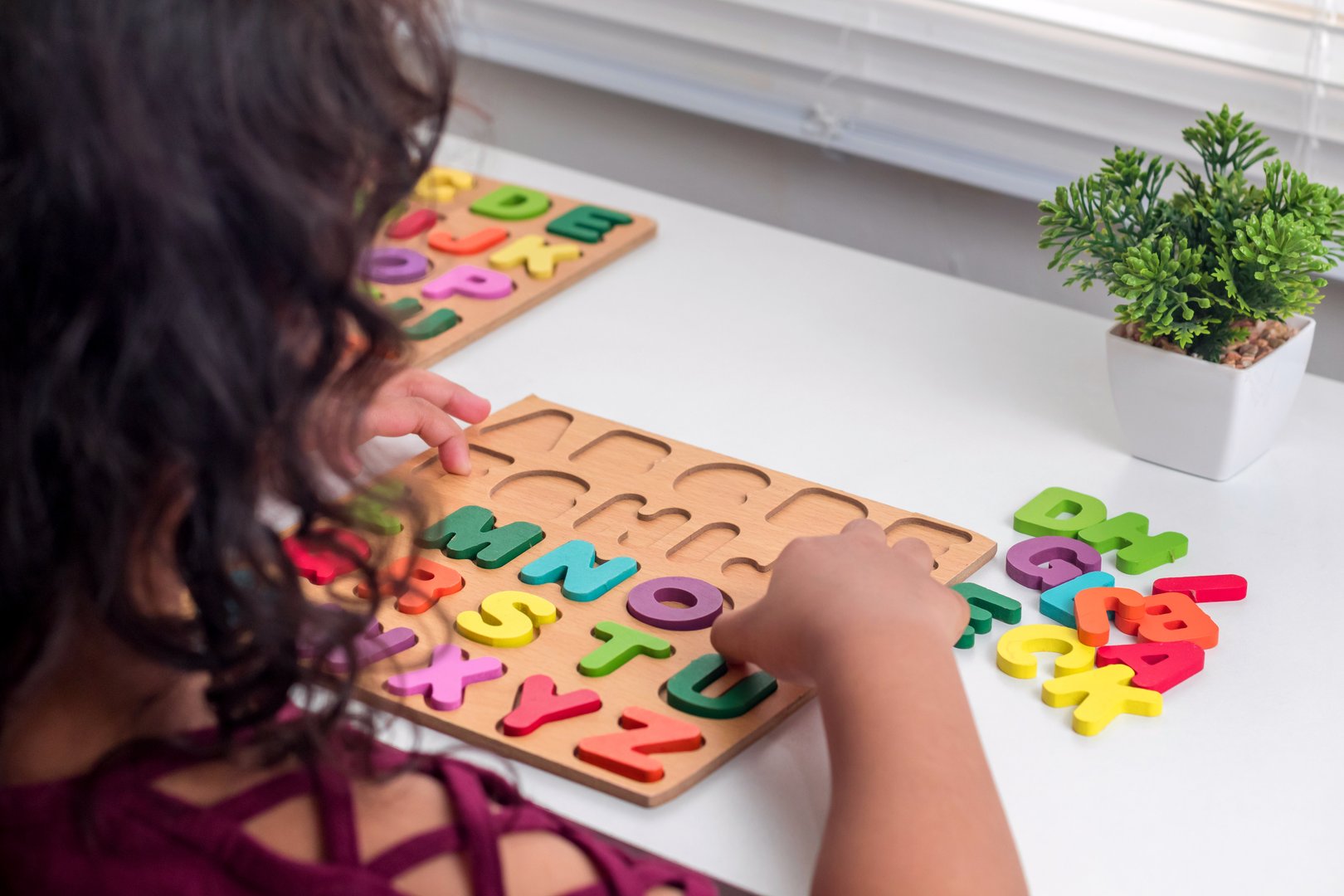 A little Asian girl plays with wooden alphabet letters puzzle on the table
