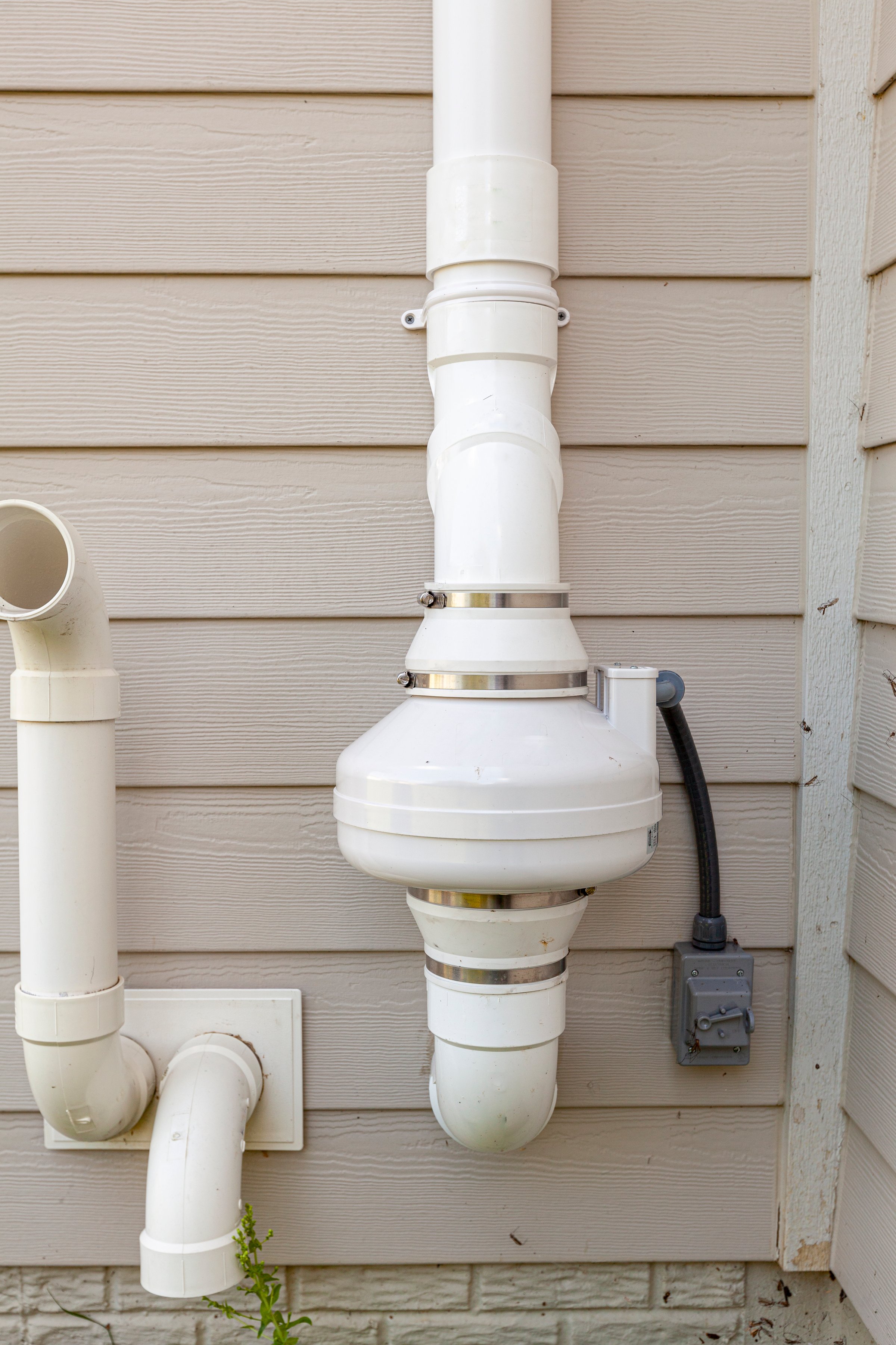 PVC pipes attached to the electrical motor of a residential radon mitigation system. TIt sucks radon rich basement ground air and removes it from the top of the house. Also helps with humidity