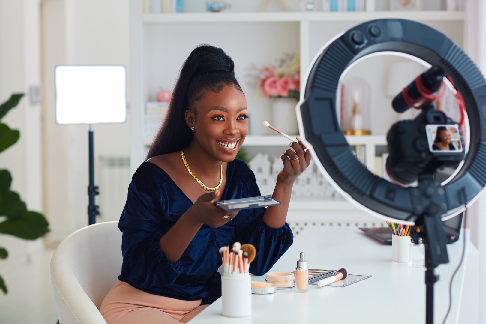happy young african american woman streaming a beauty vlog from home, online content creator applying a makeup on