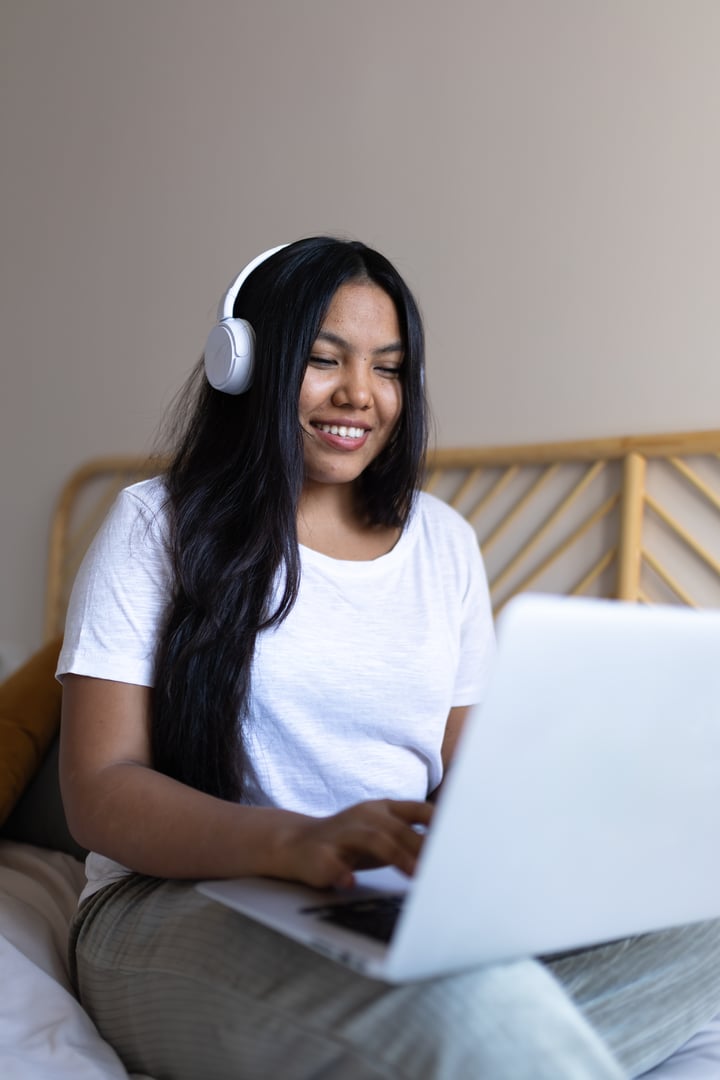 Smiling young woman working from home using laptop and headphones