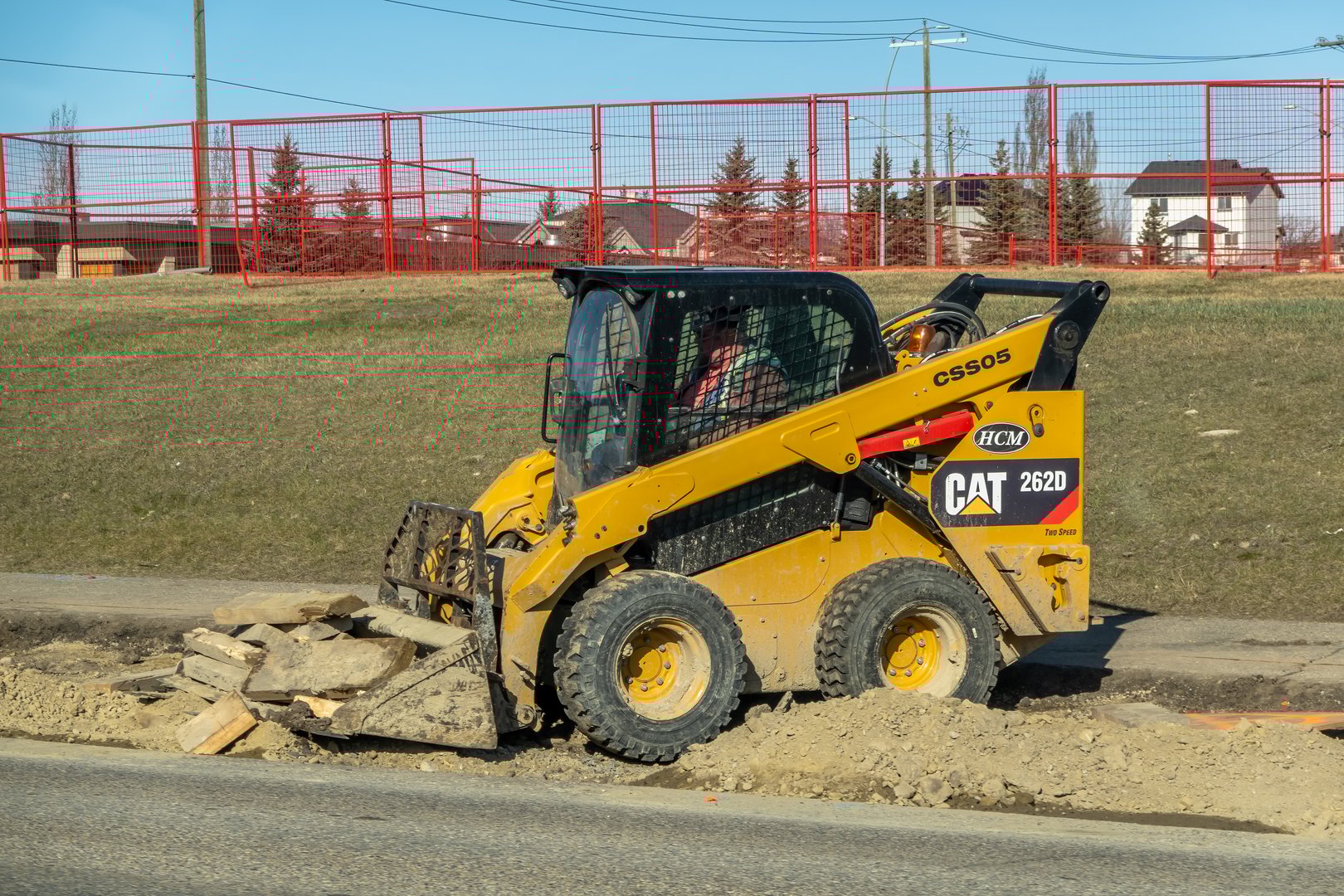 Calgary, Alberta, Canada. Apr 14, 2025. A yellow Caterpillar 262D skid-steer loader is shown at work on a construction site, moving earth and rocks.