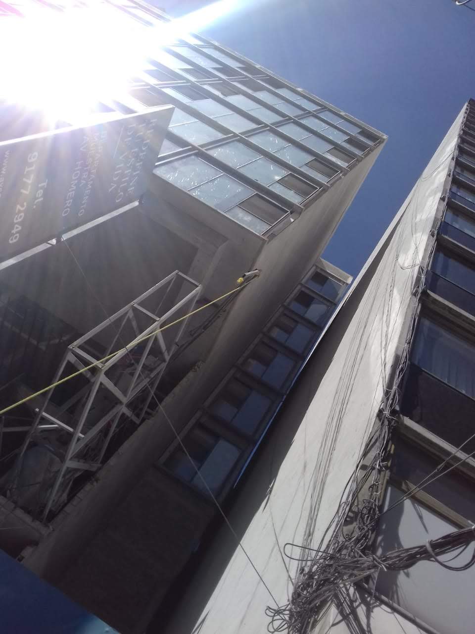 Tall buildings with large windows, sunlight creating lens flare, construction equipment and cables visible on the façades.