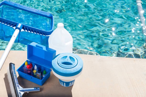 Pool cleaning tools including skimmer net, test kit, and chlorine floater by a residential pool