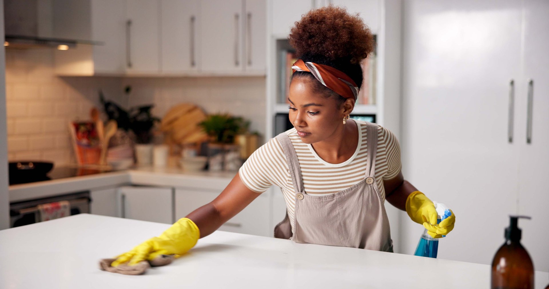 Woman, cloth and wipe on kitchen counter for hygiene with spray, gloves or chemical for shine in home. Person, cleaning and bottle for dust, dirt or bacteria with sanitation, liquid or task in house