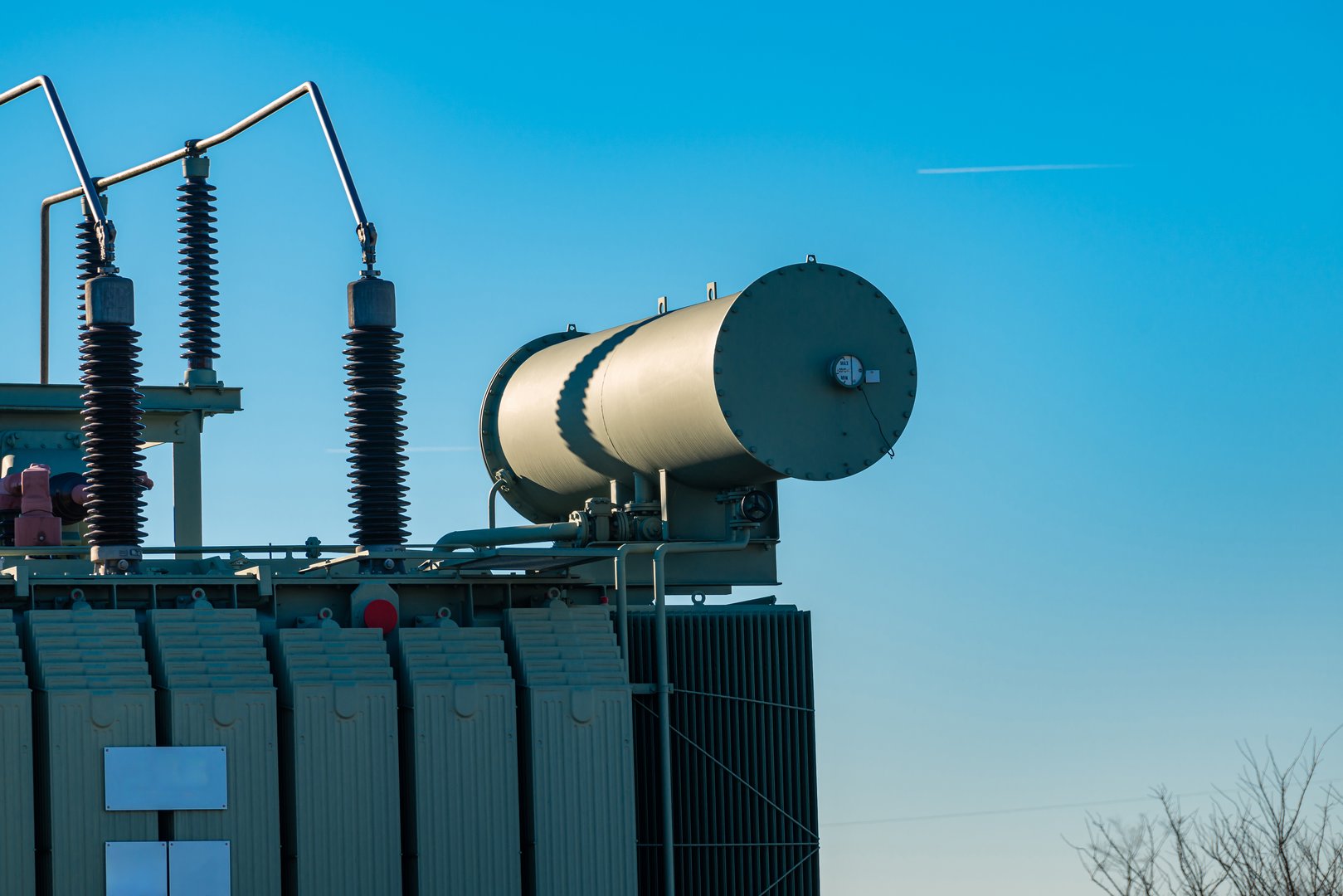 An industrial transformer is prominently displayed under a bright blue sky.