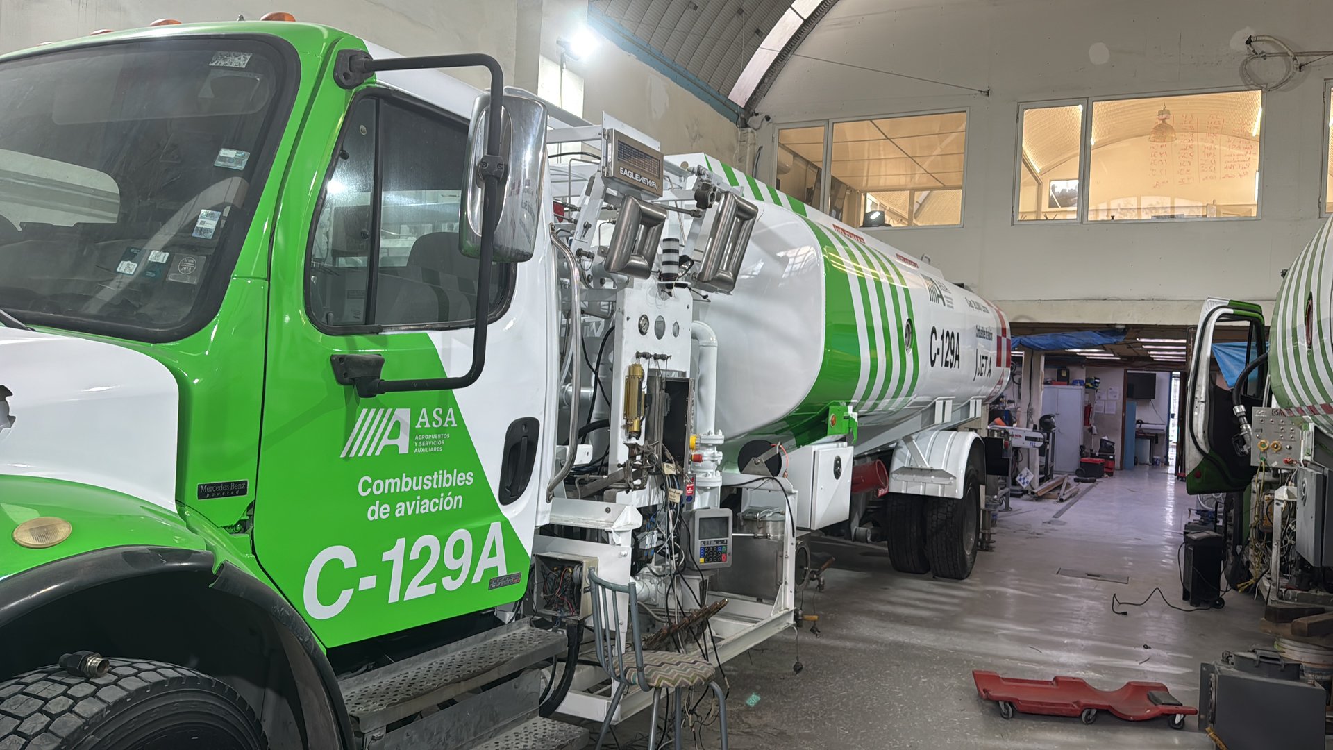 Aviation fuel truck inside a maintenance garage with tools and equipment visible in the background.