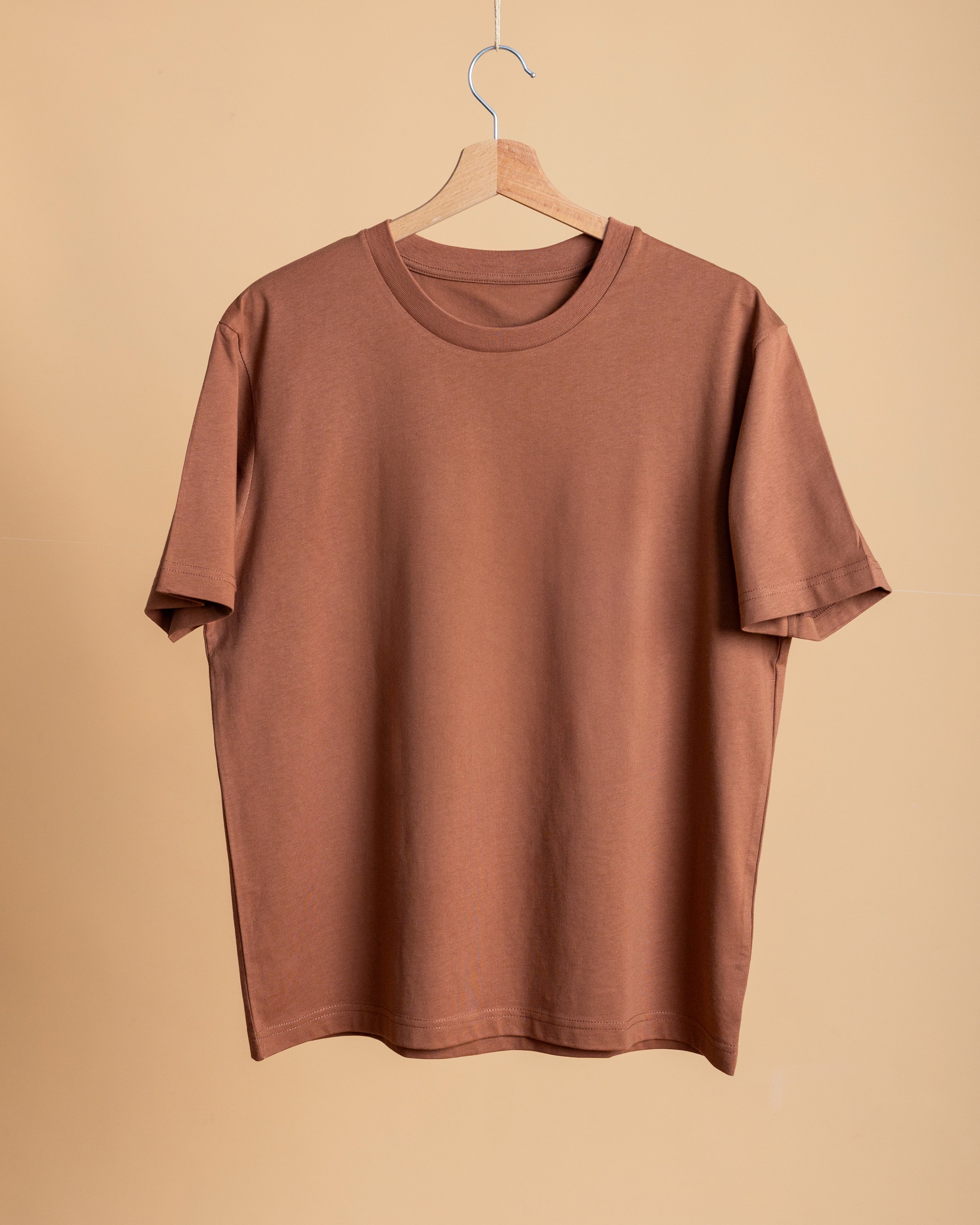 Blank terracotta-colored T-shirt on a uniform beige background. Studio quality photography for apparel and graphic presentations.