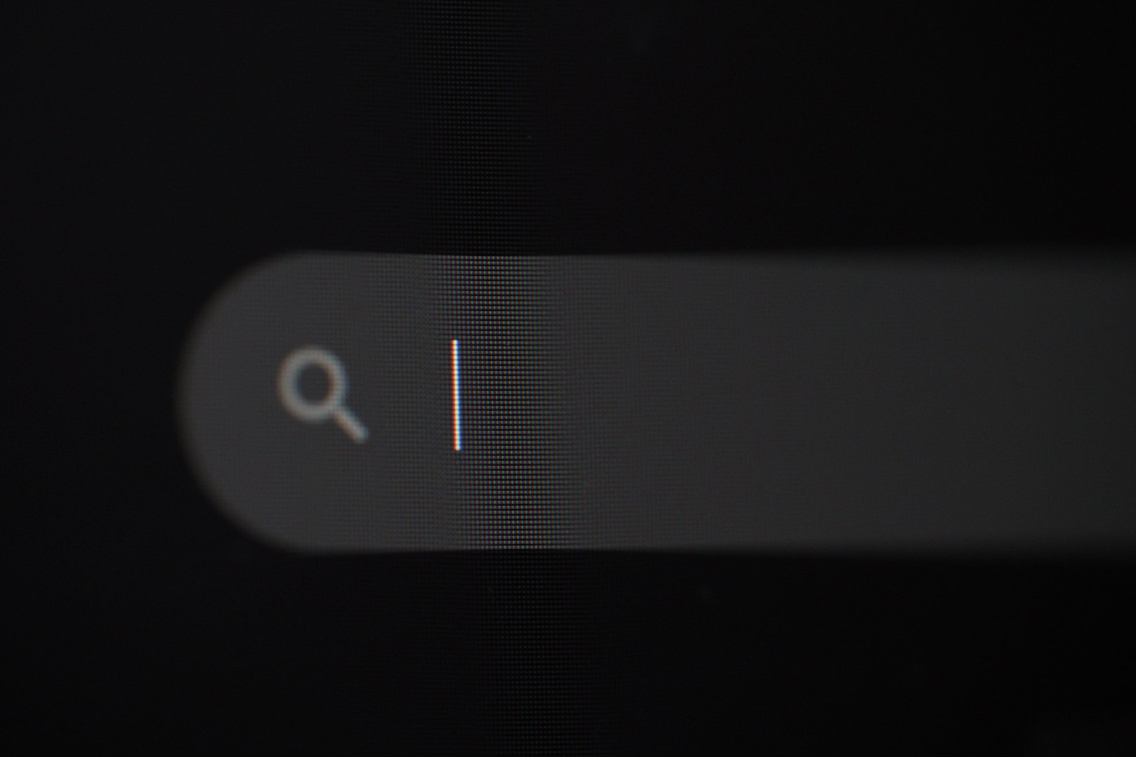 Close-up of a search bar icon with a blinking cursor, showing the interface of an online search tool on a dark background.
