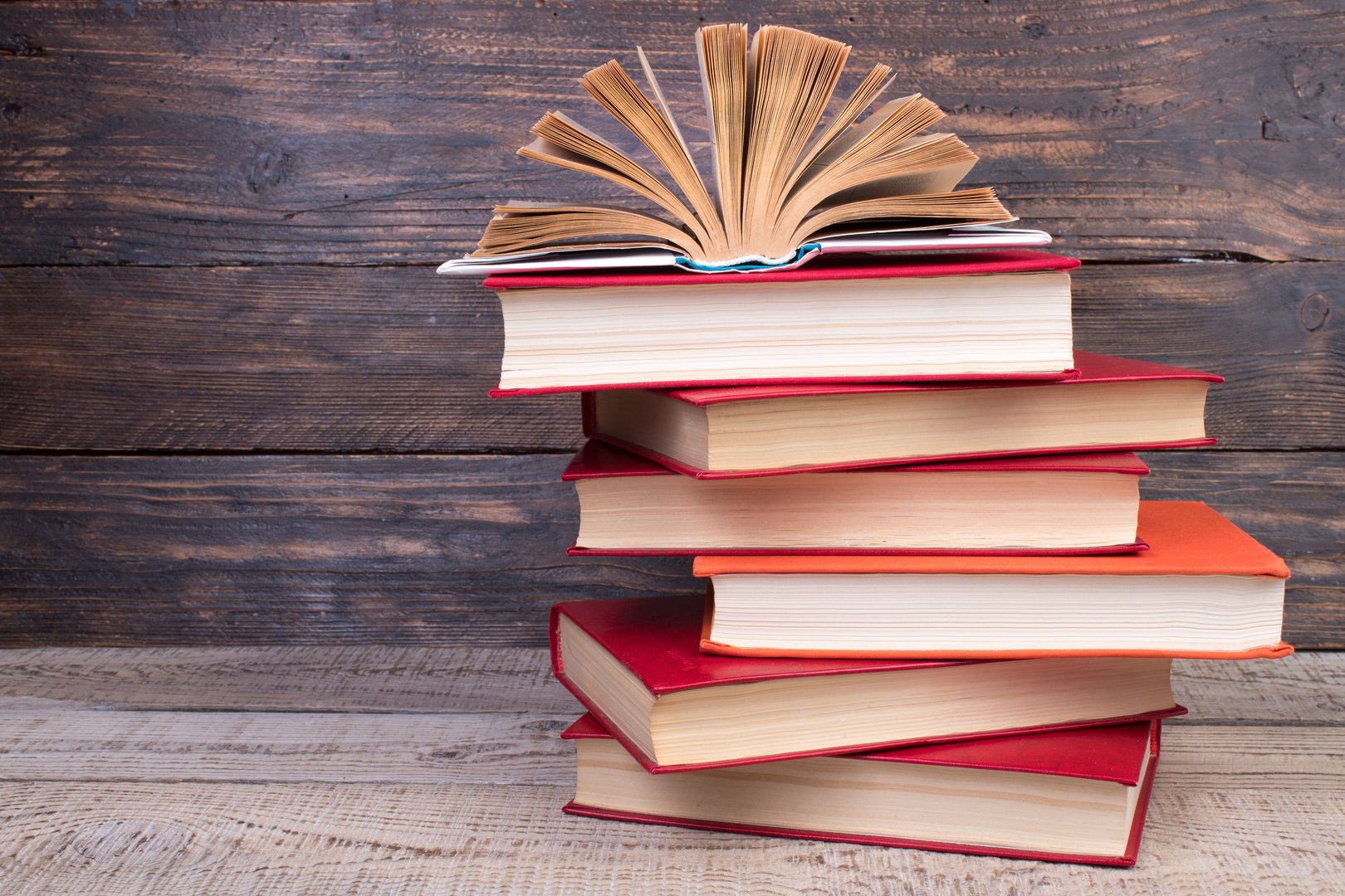 Composition with hardback books, fanned pages on wooden deck table and background. Books stacking. Back to school. Copy Space. Education background