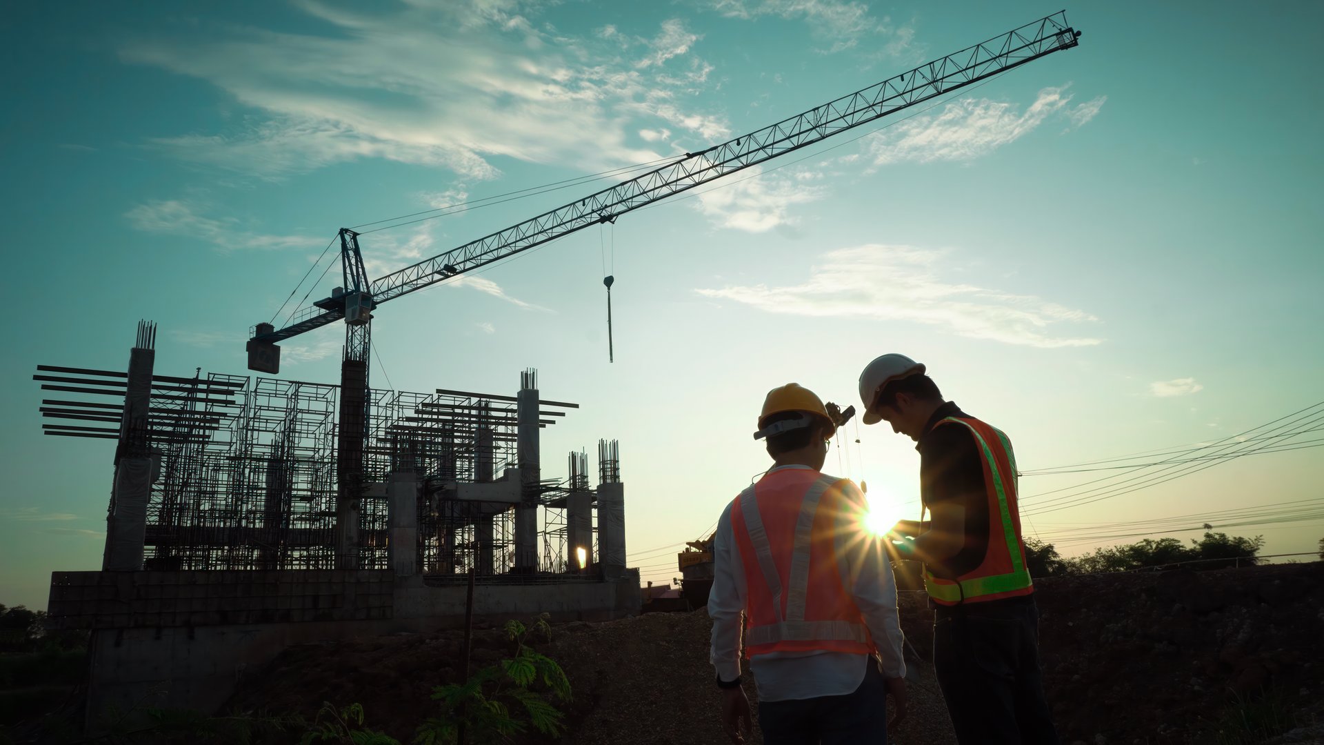 Silhouette of team engineer using laptop to control work, crane, construction site.
