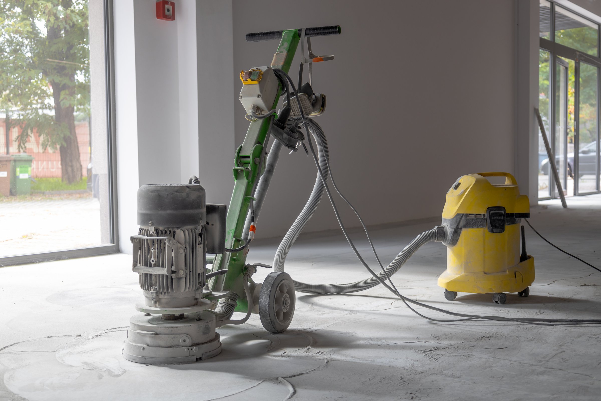 Professional concrete floor grinder, vacuum cleaner connected to the grinder, industrial concrete floor grinding.