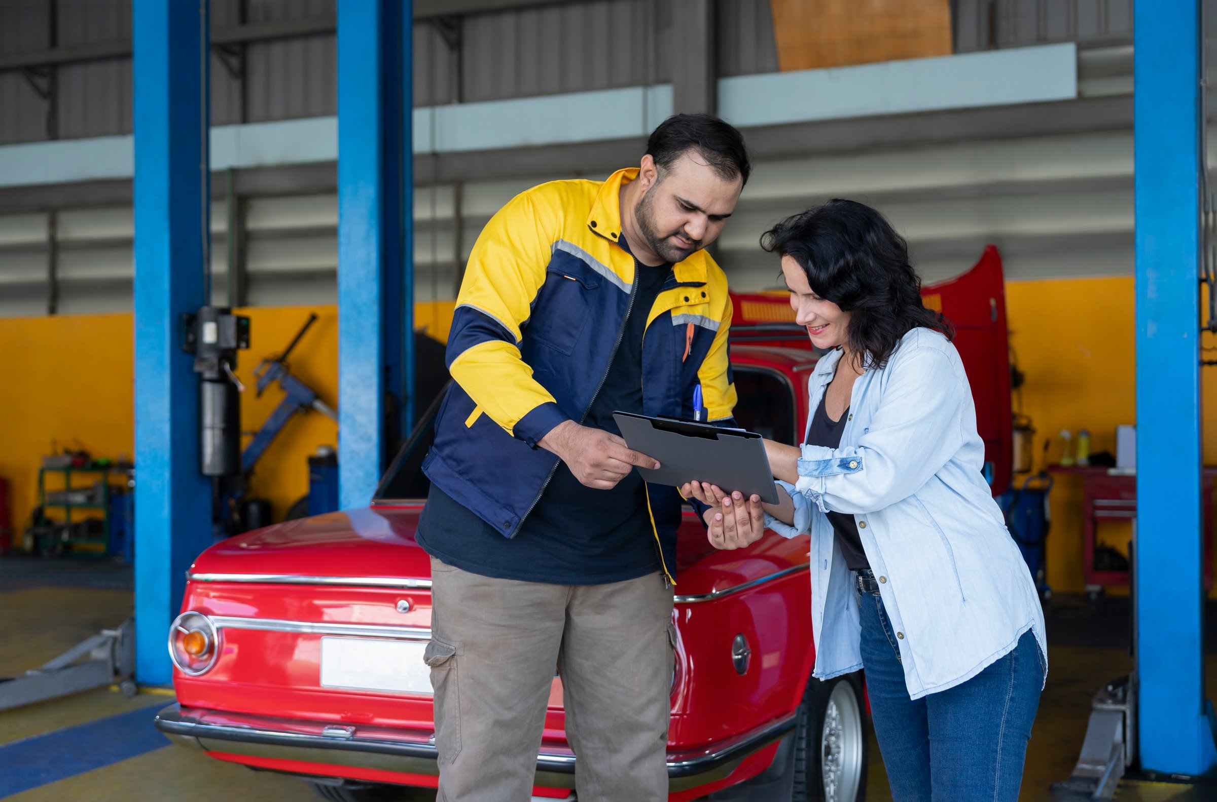 asian mechanic male is holding clipboard send to a caucasian customer sign a quotation before proceeding to repair a car at the garage