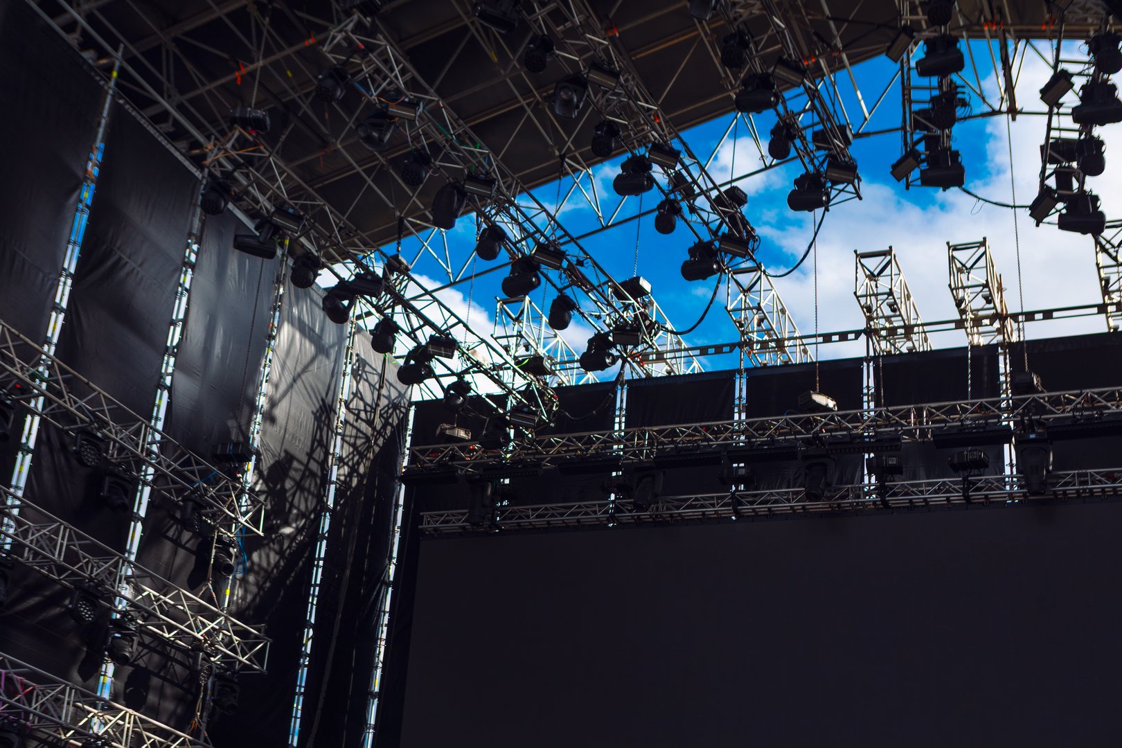 Stage setup with metal scaffolding, spotlights and lighting equipment against blue sky. Structure highlights preparations for a concert or outdoor event