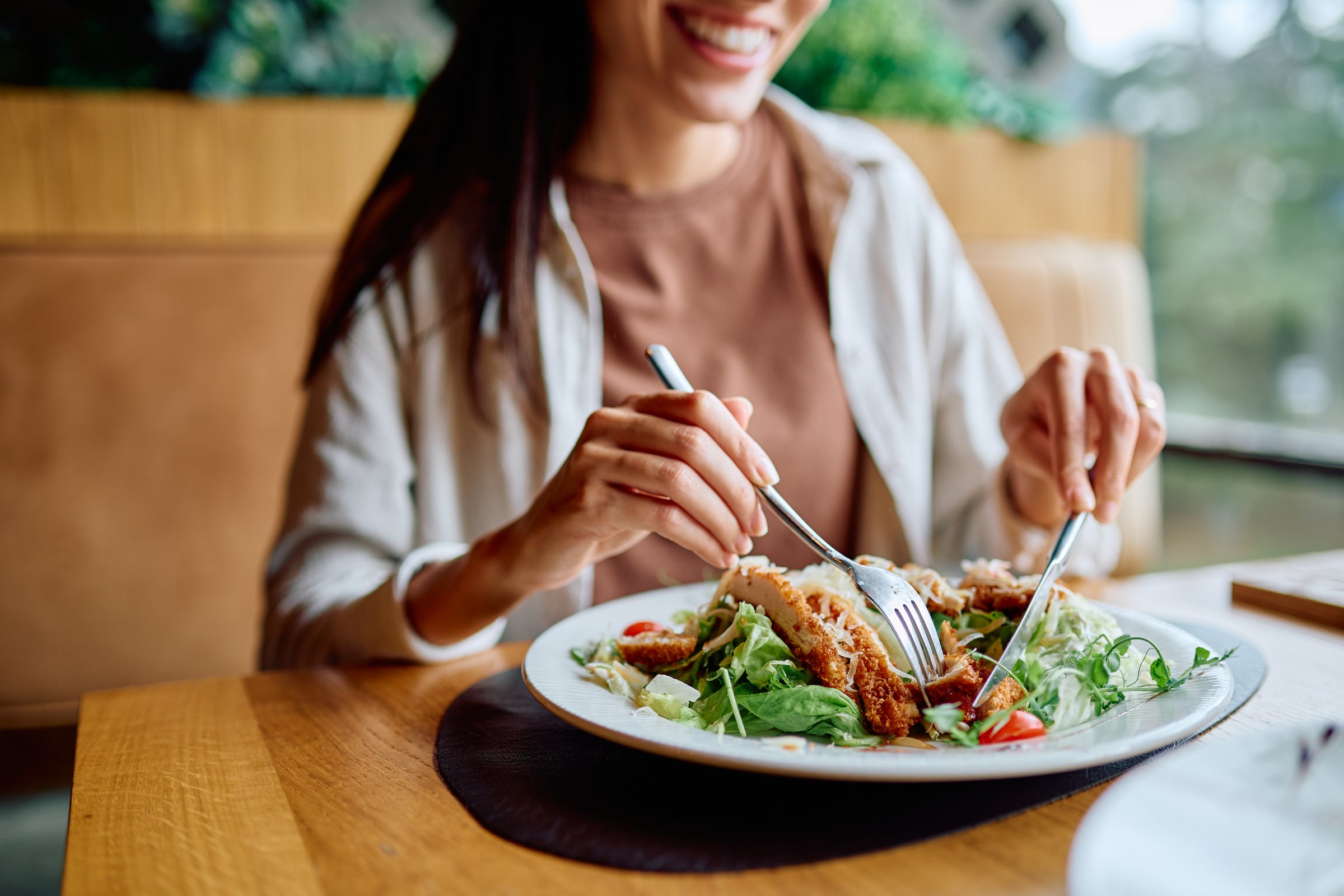 Woman smiling, eating fresh chicken salad in a restaurant. Promoting healthy eating, lunch, diet, wellness, and lifestyle